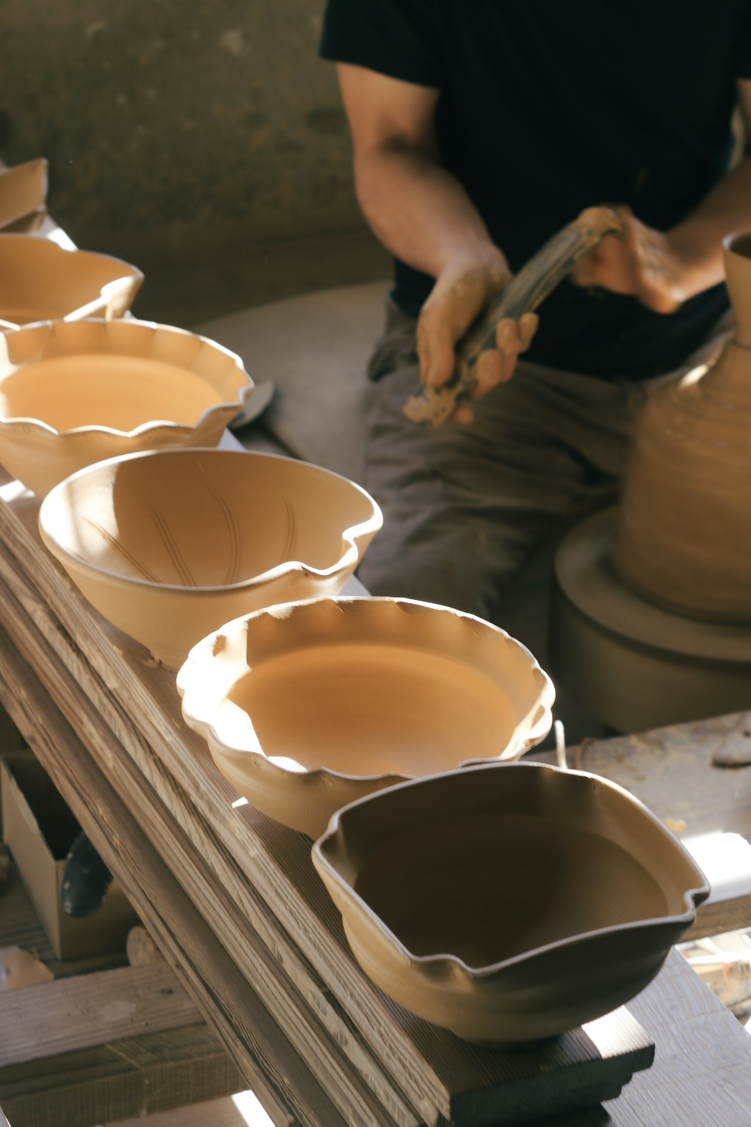 Potter shaping clay bowls and a vase with pottery in progress