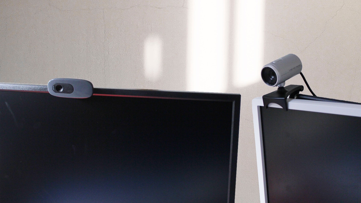 Dua monitor komputer dengan webcam terpasang dan bayangan cahaya terang