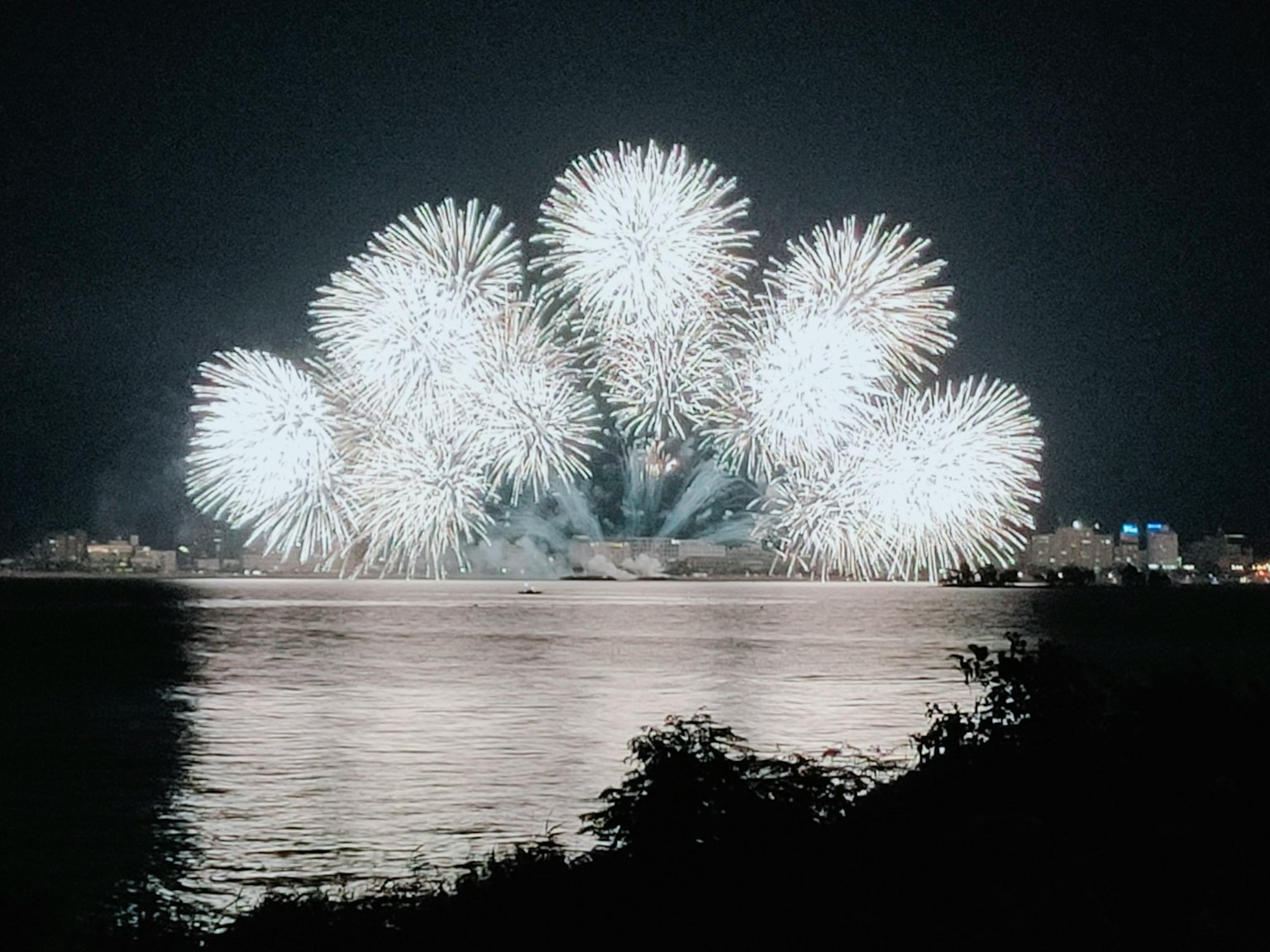 White fireworks bursting in the night sky reflected on water