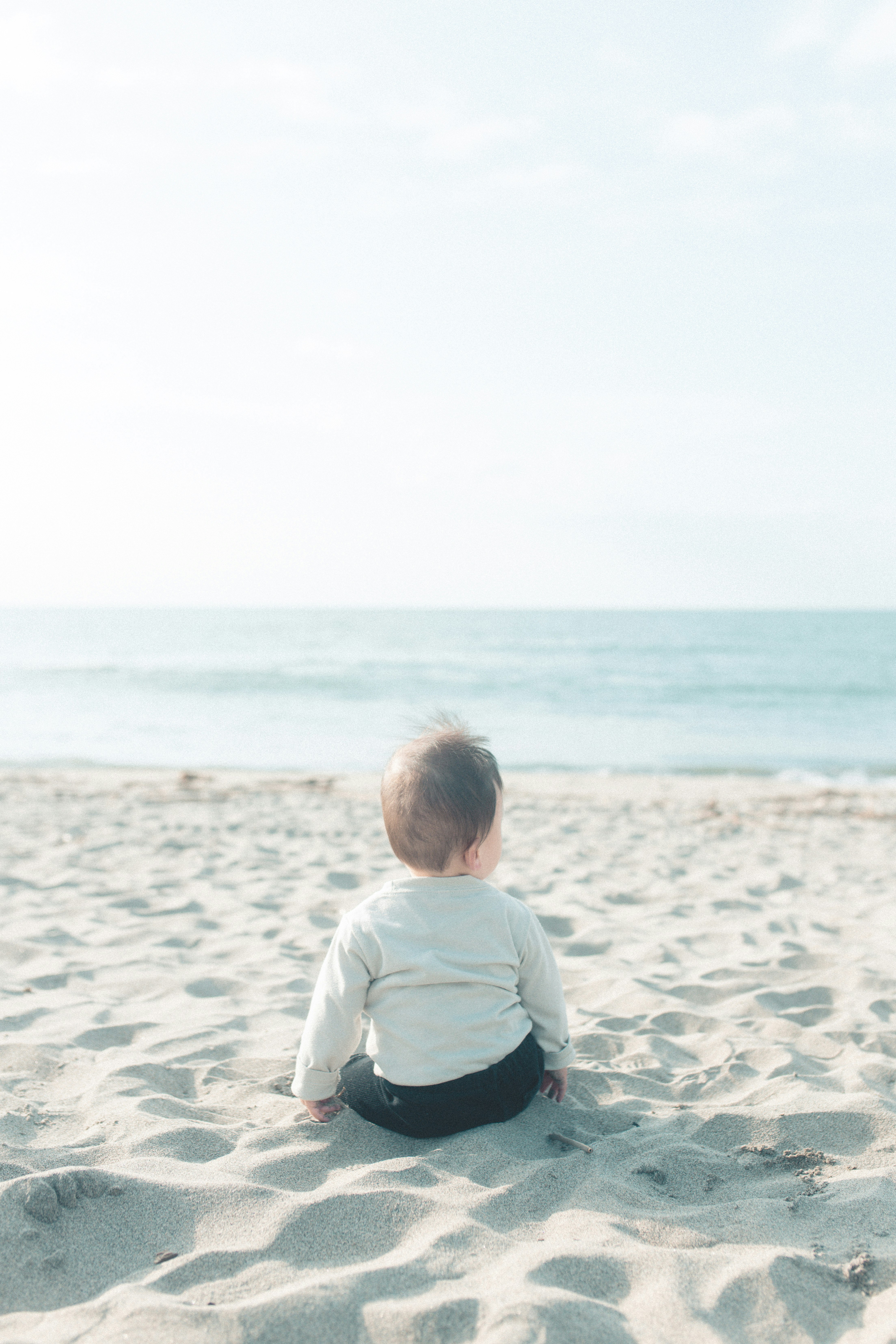 Baby sitting on the sand facing the ocean