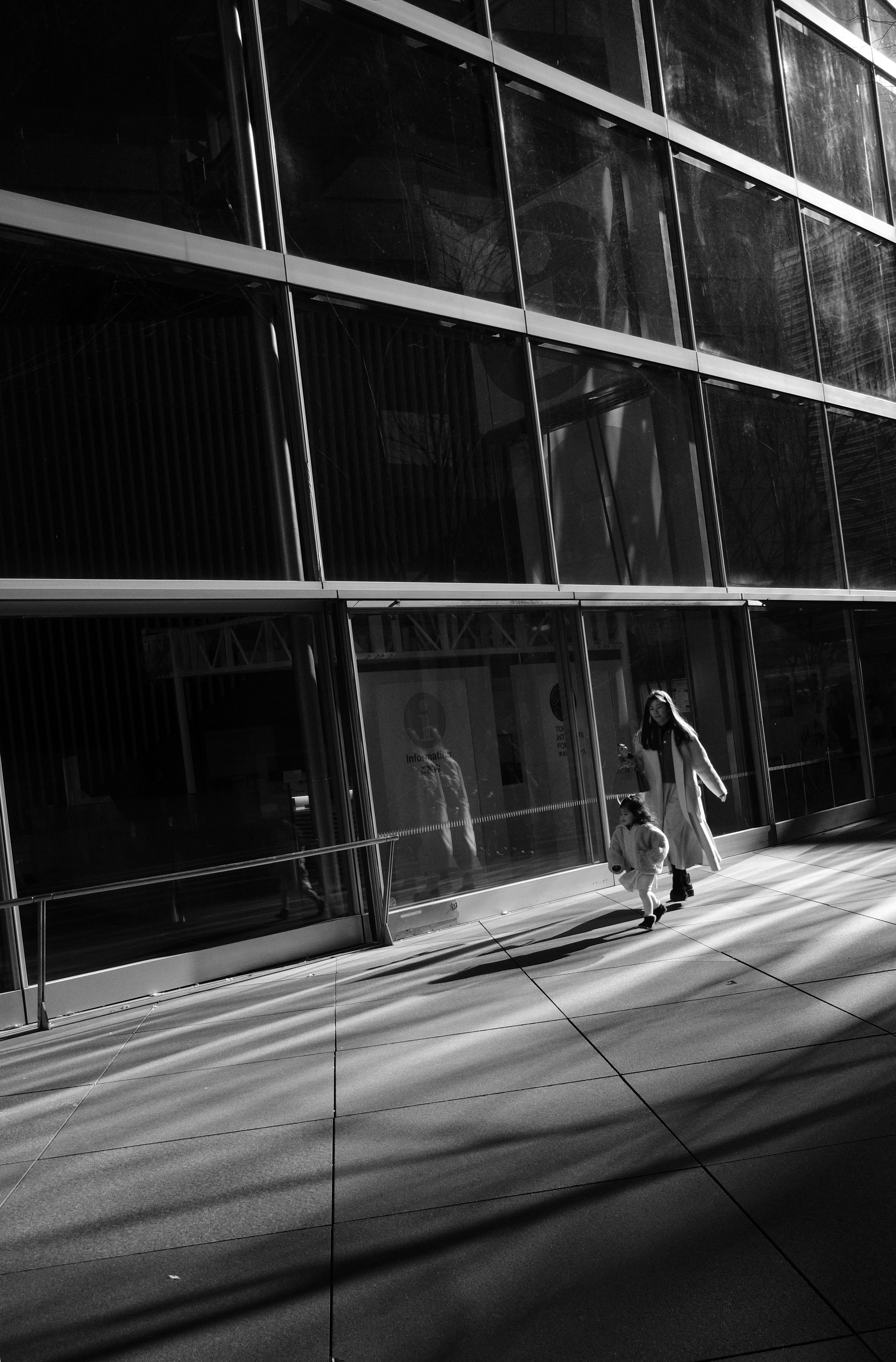 ガラス張りの建物の外壁と歩く人のある通路