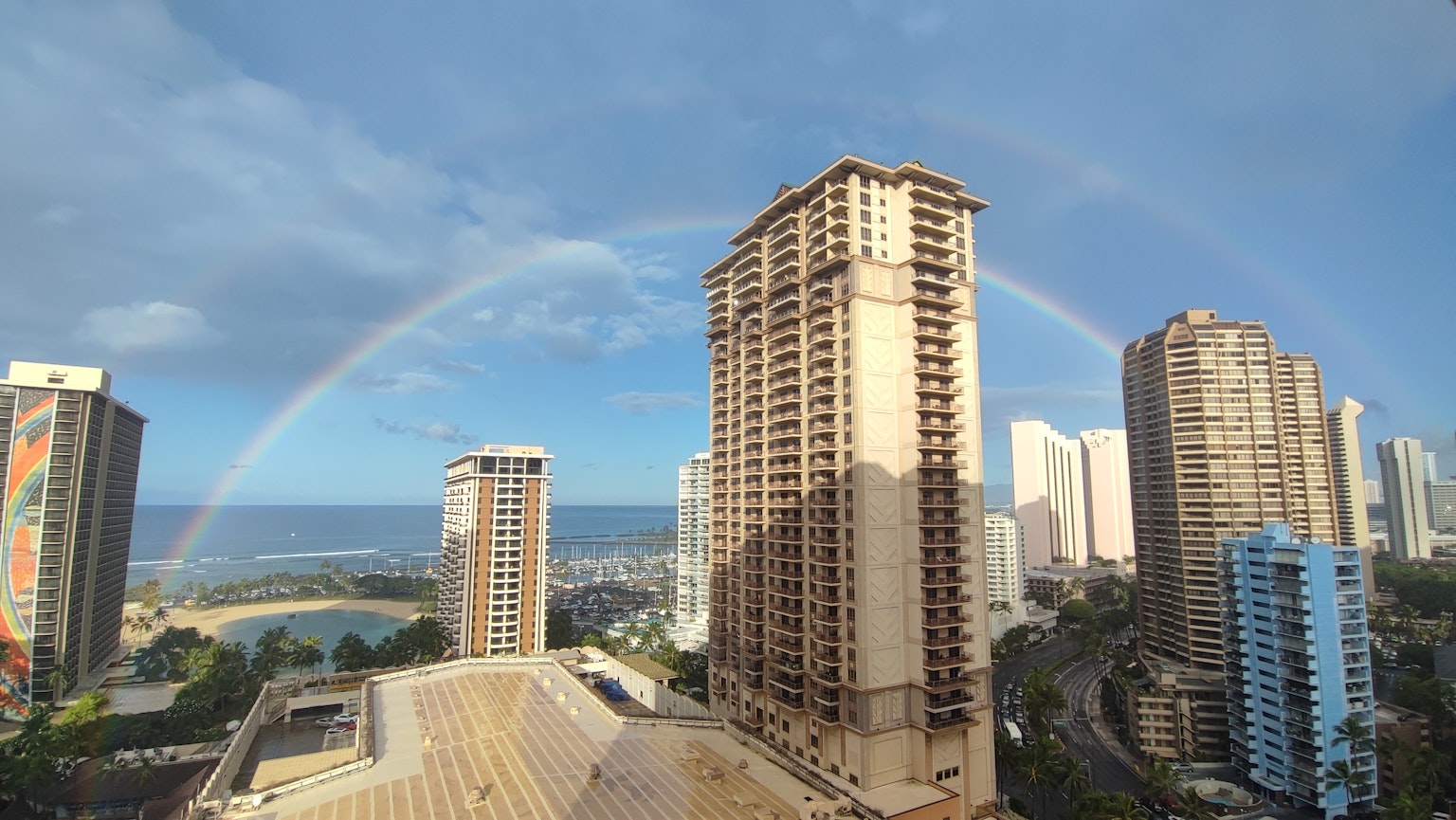 Rainbow arching over skyscrapers in Hawaii with a blue sky