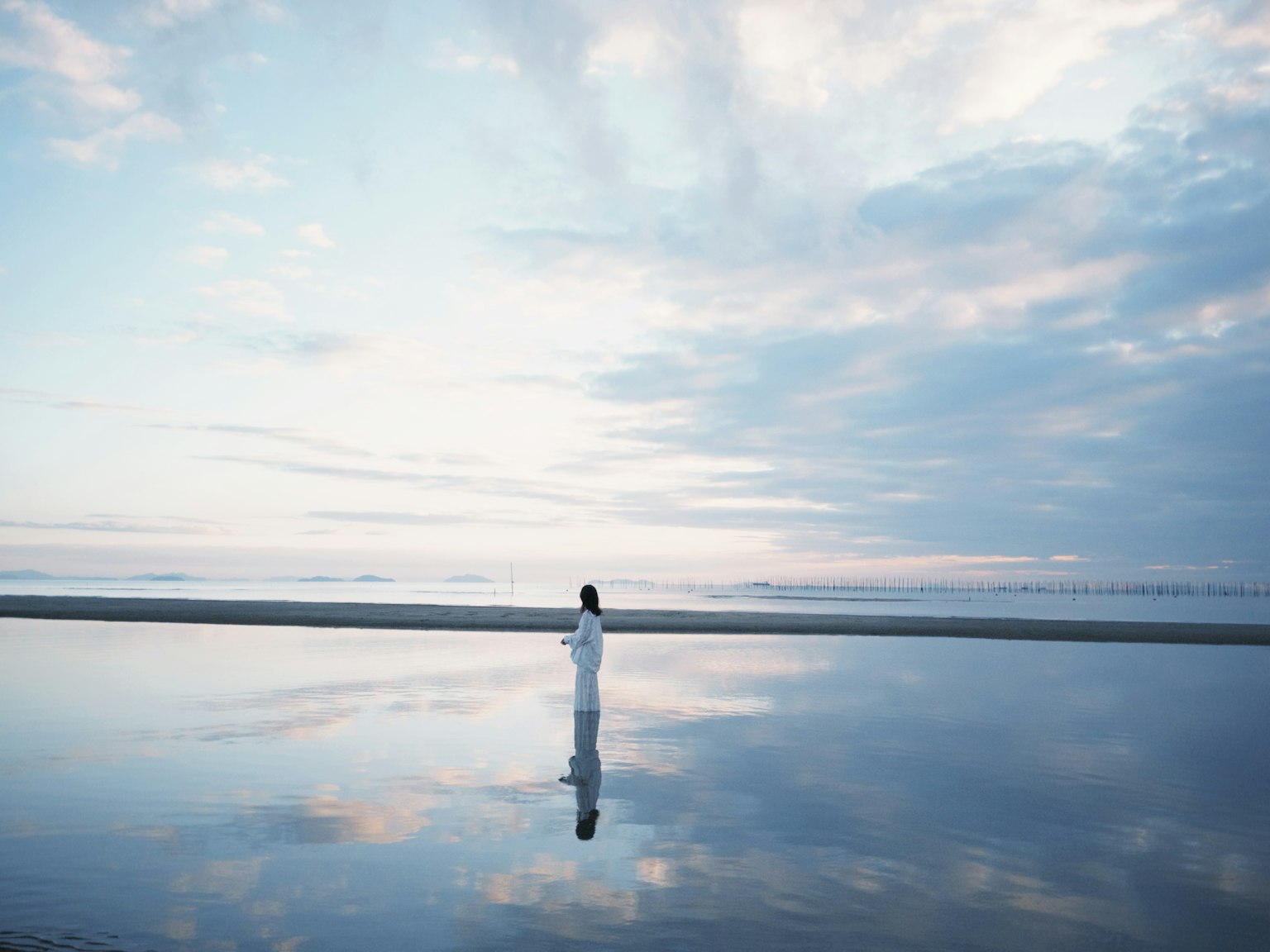 Person in white standing on reflective water surface under a cloudy sky