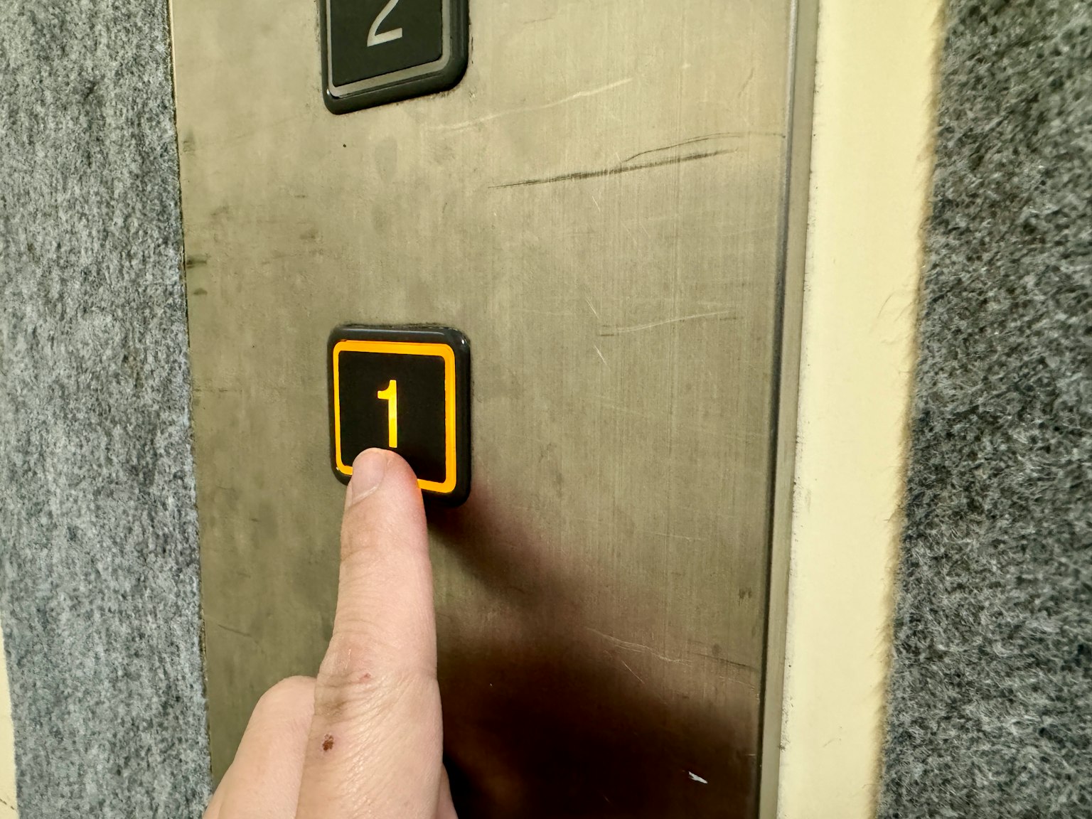 Dedo presionando el botón del ascensor número 1 en un panel metálico