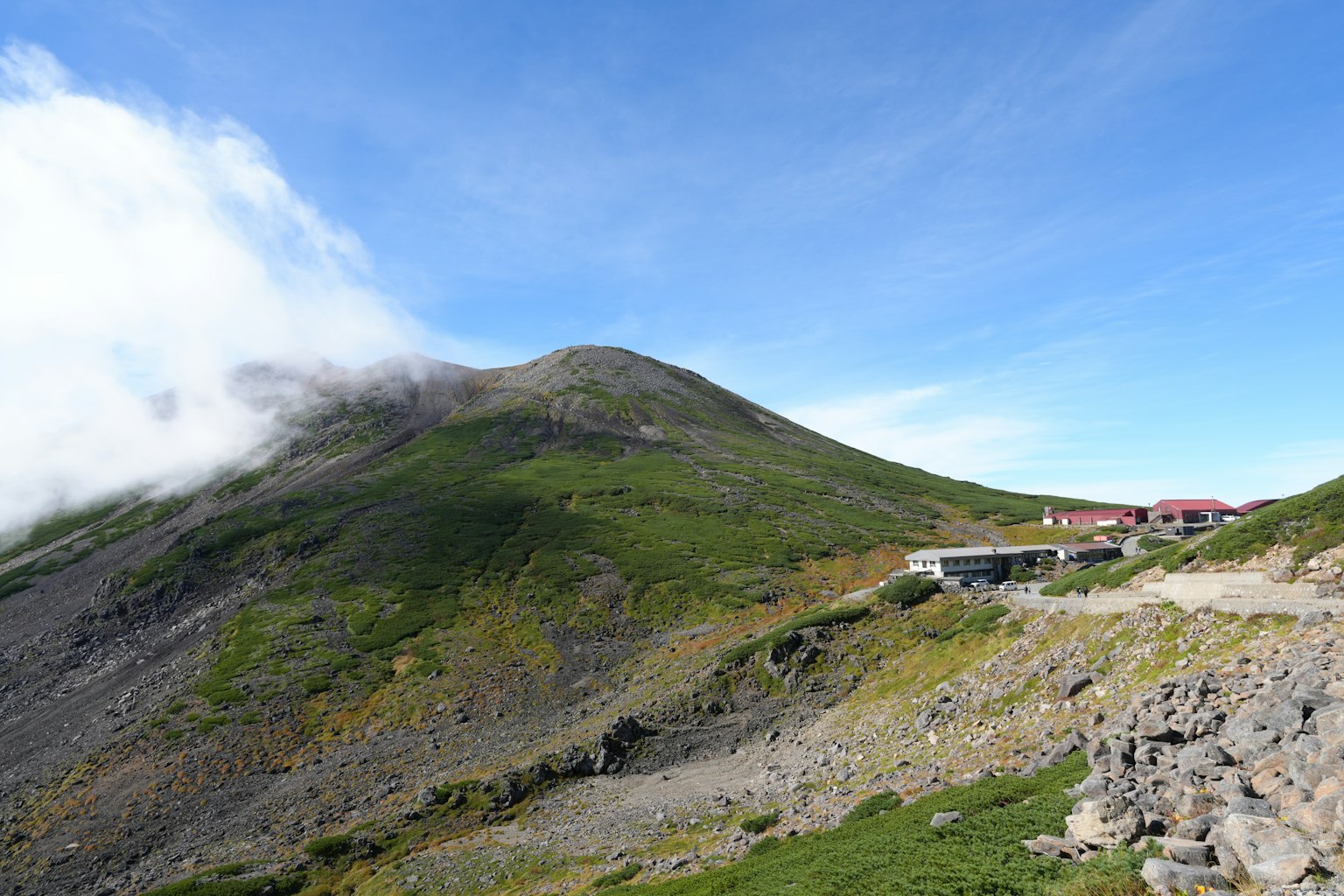 Scenic view of a green mountain under a blue sky with a mountain hut
