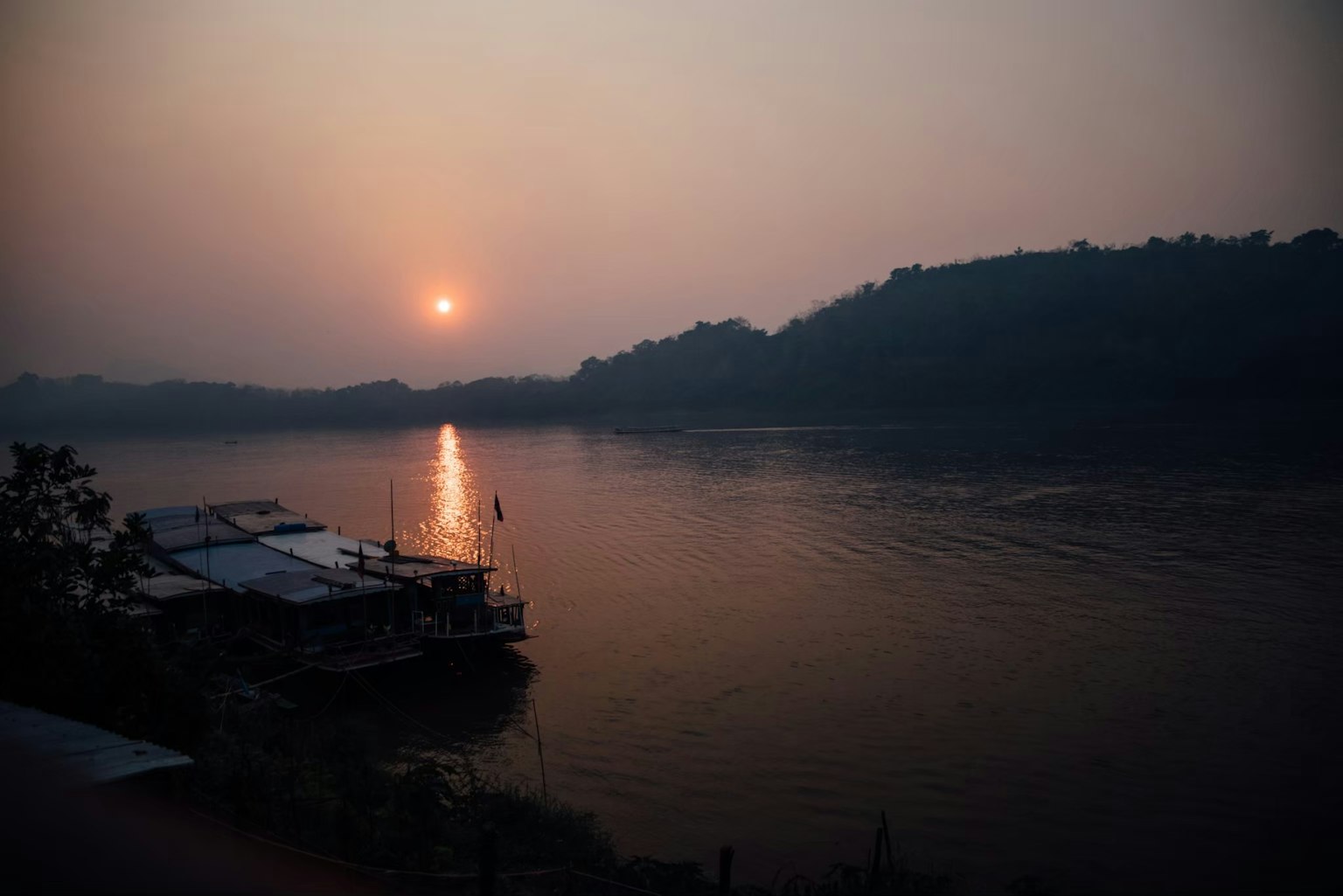 Pemandangan matahari terbenam di atas sungai dengan siluet perbukitan