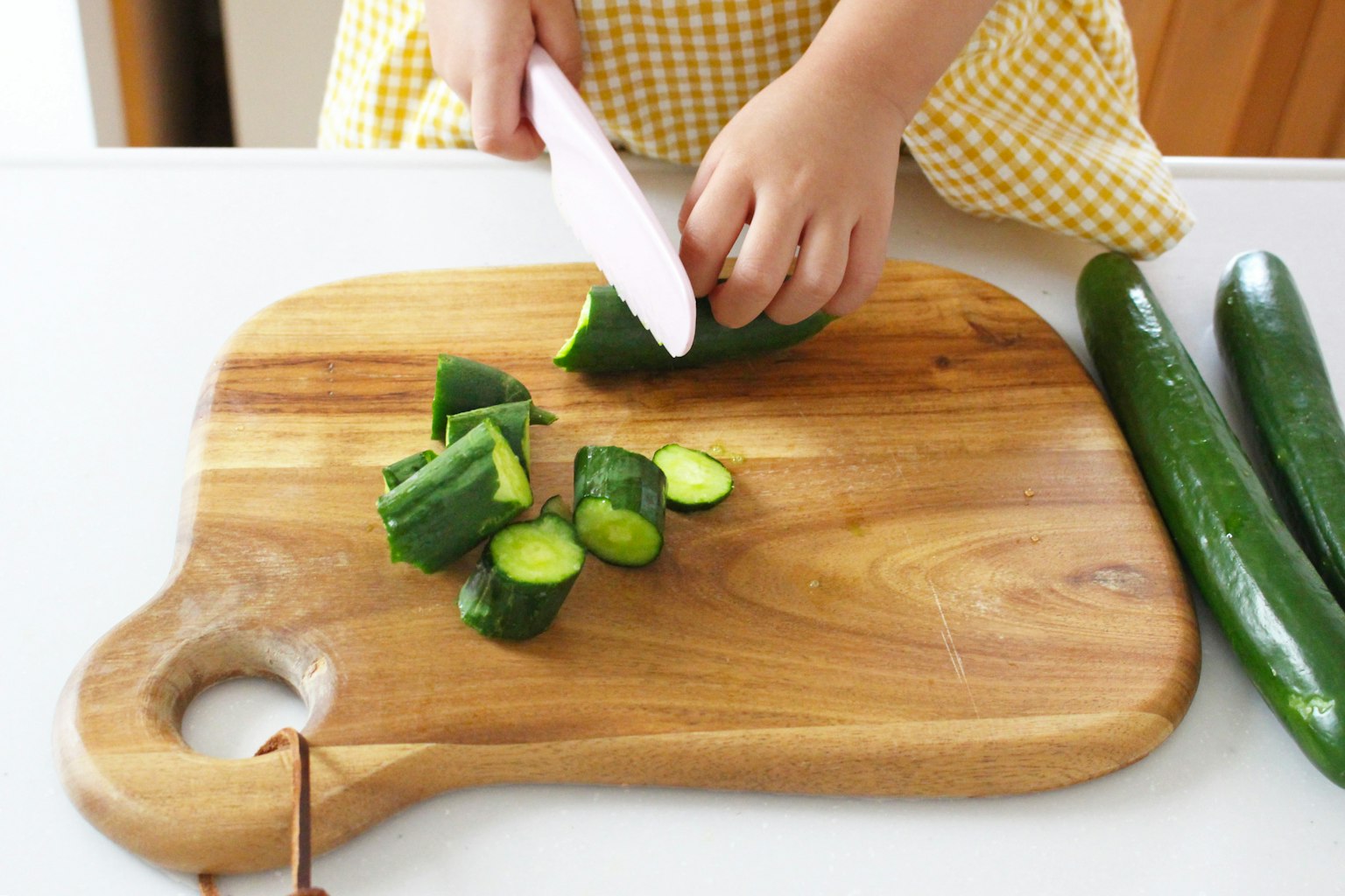 Main d'enfant coupant un concombre sur une planche à découper en bois