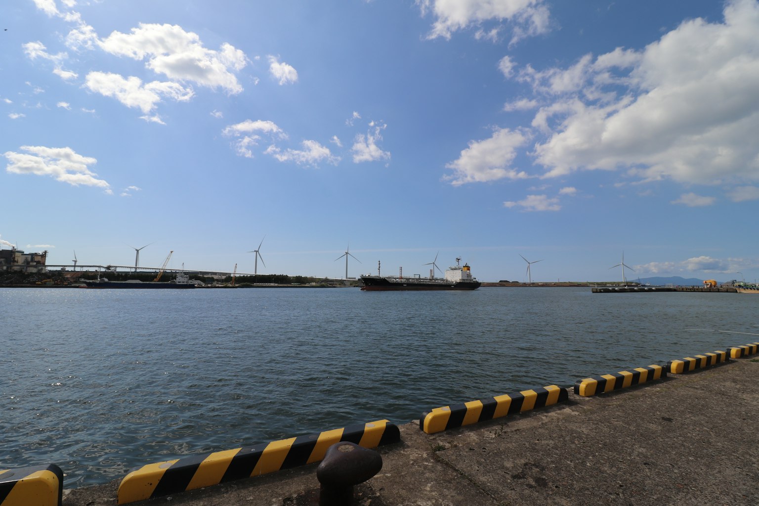 Eine Hafenszene mit einem Schiff, das im blauen Wasser unter einem Himmel mit weißen Wolken liegt