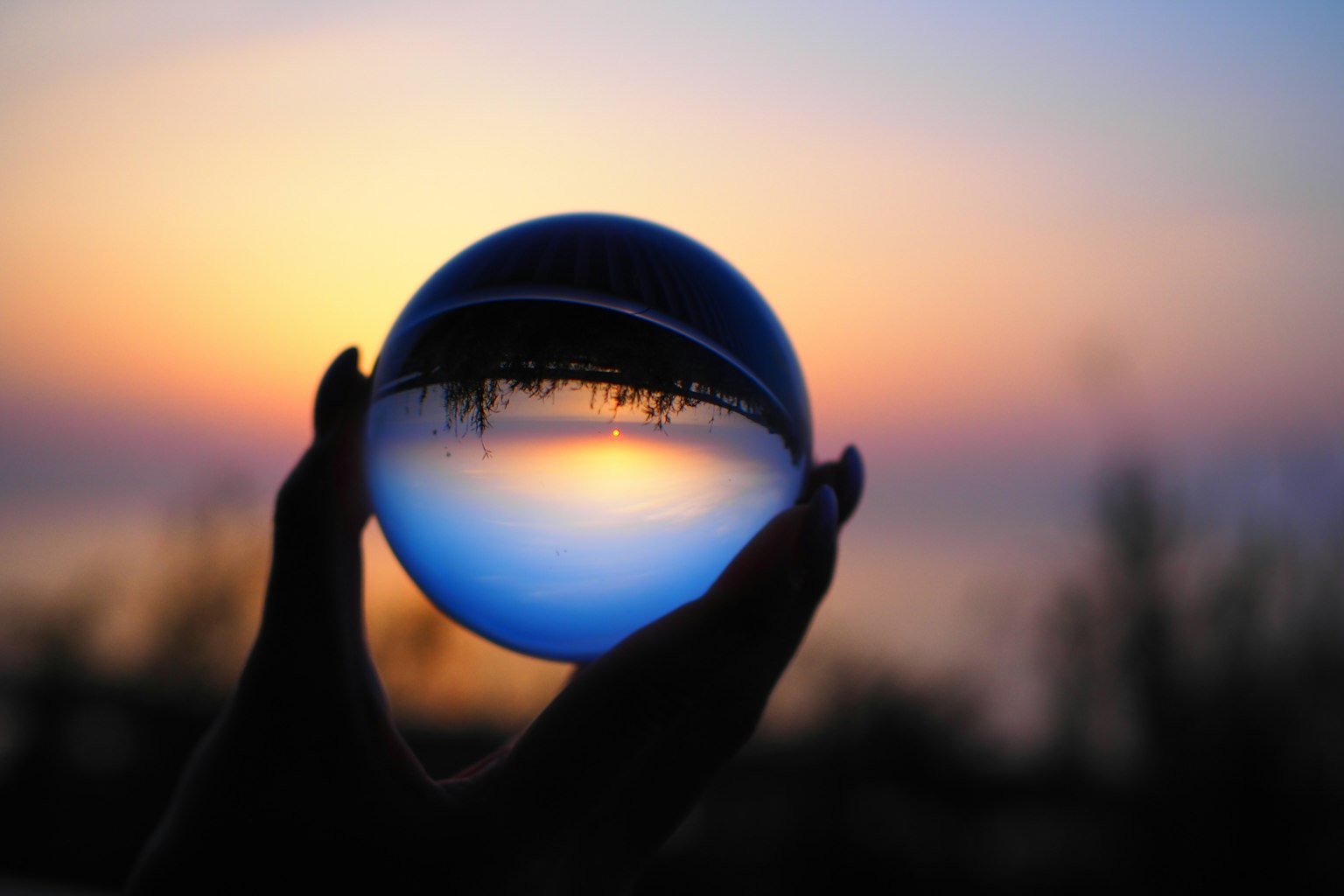 Una bola de cristal sostenida en la mano que refleja un atardecer