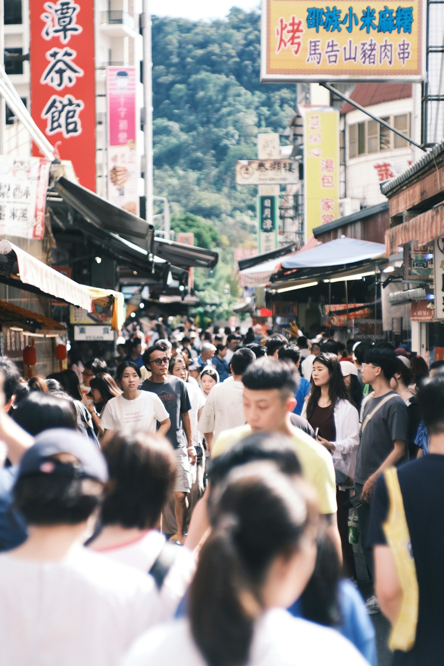 Überfüllte Marktstraße voller Menschen verschiedene Schilder und ein bergiger Hintergrund