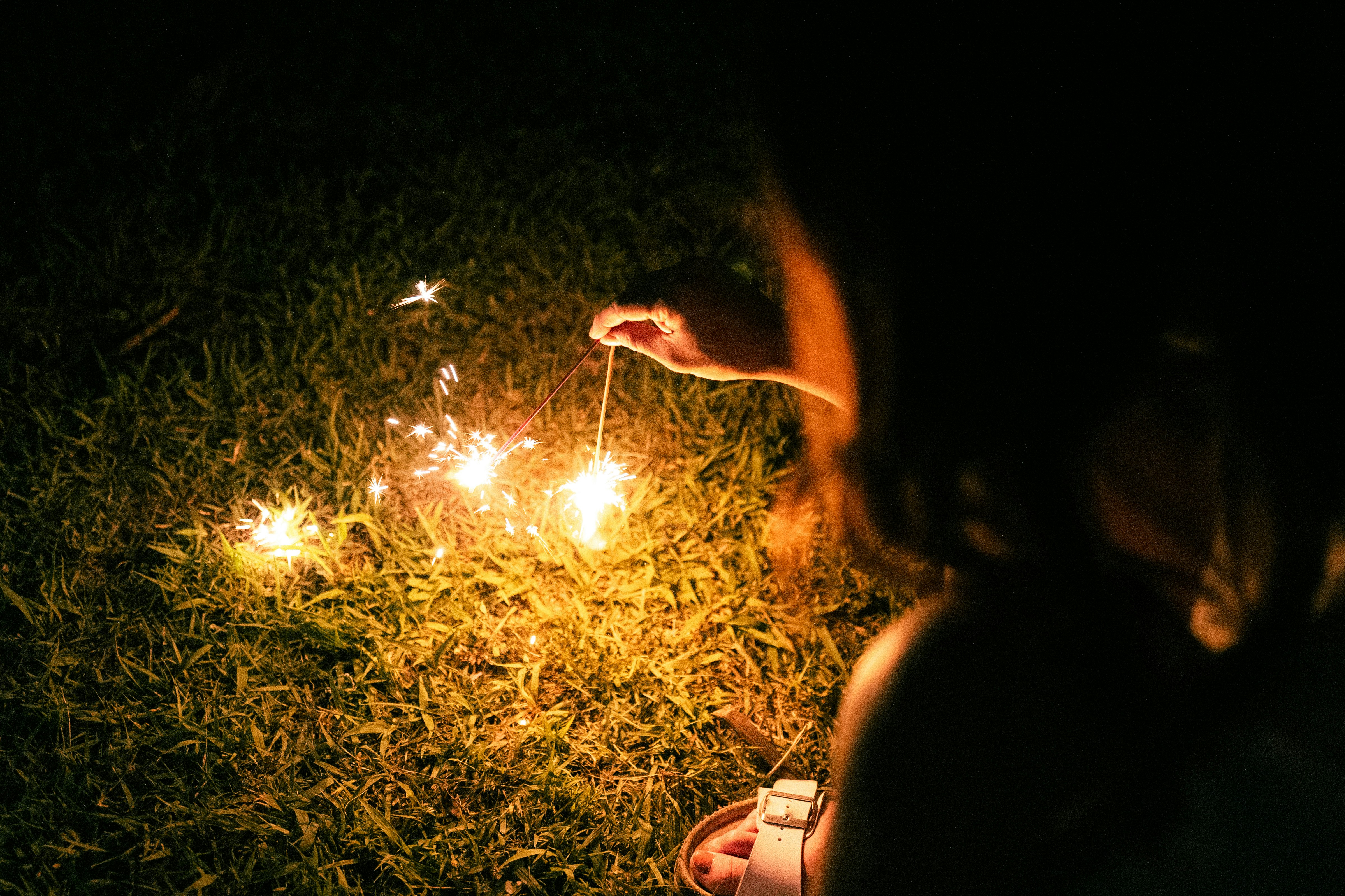 hands holding sparklers on grass