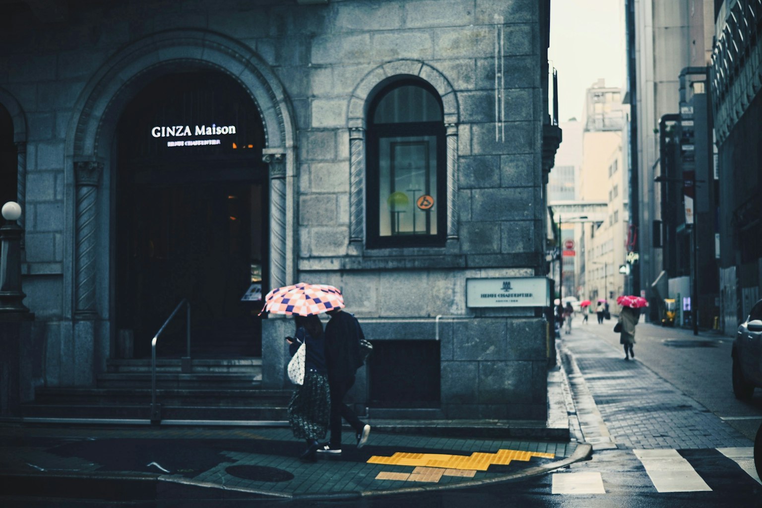 People walking with umbrellas in the rain near a historic building