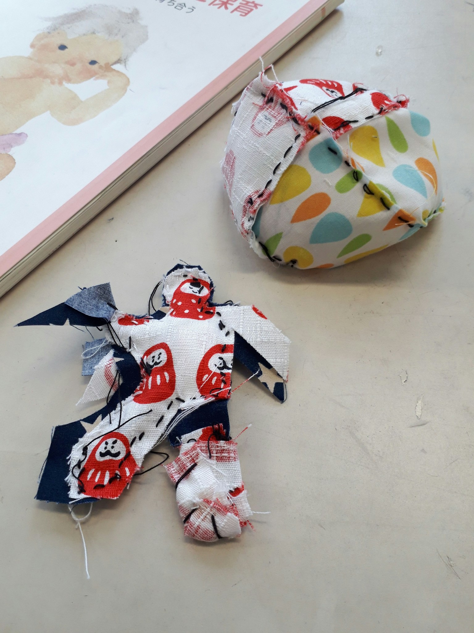 Una piccola bambola con motivi di daruma rossi e una palla di tessuto a pois colorati sono posizionate affiancate