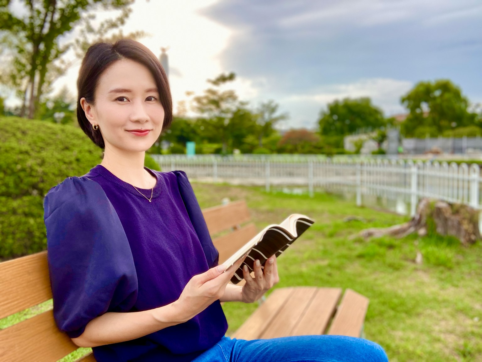 ภาพถ่ายของผู้หญิงนั่งอยู่บนม้านั่งในสวนถือหนังสือ