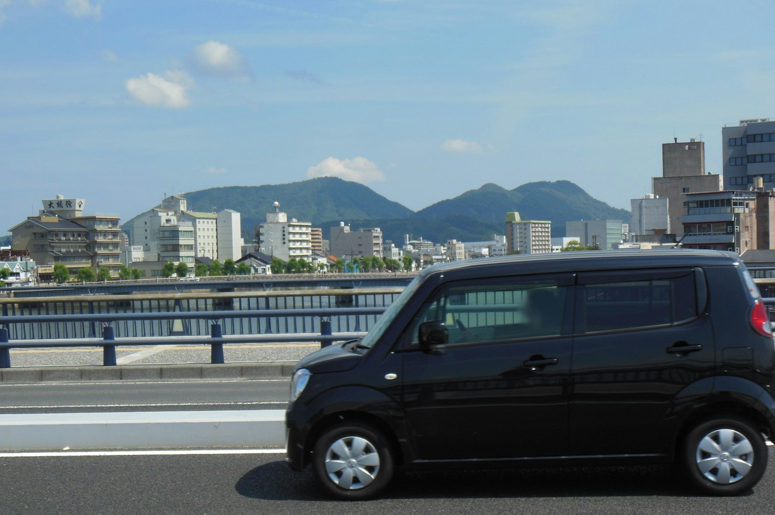 Auto nera che circola su un'autostrada con skyline urbano e montagne