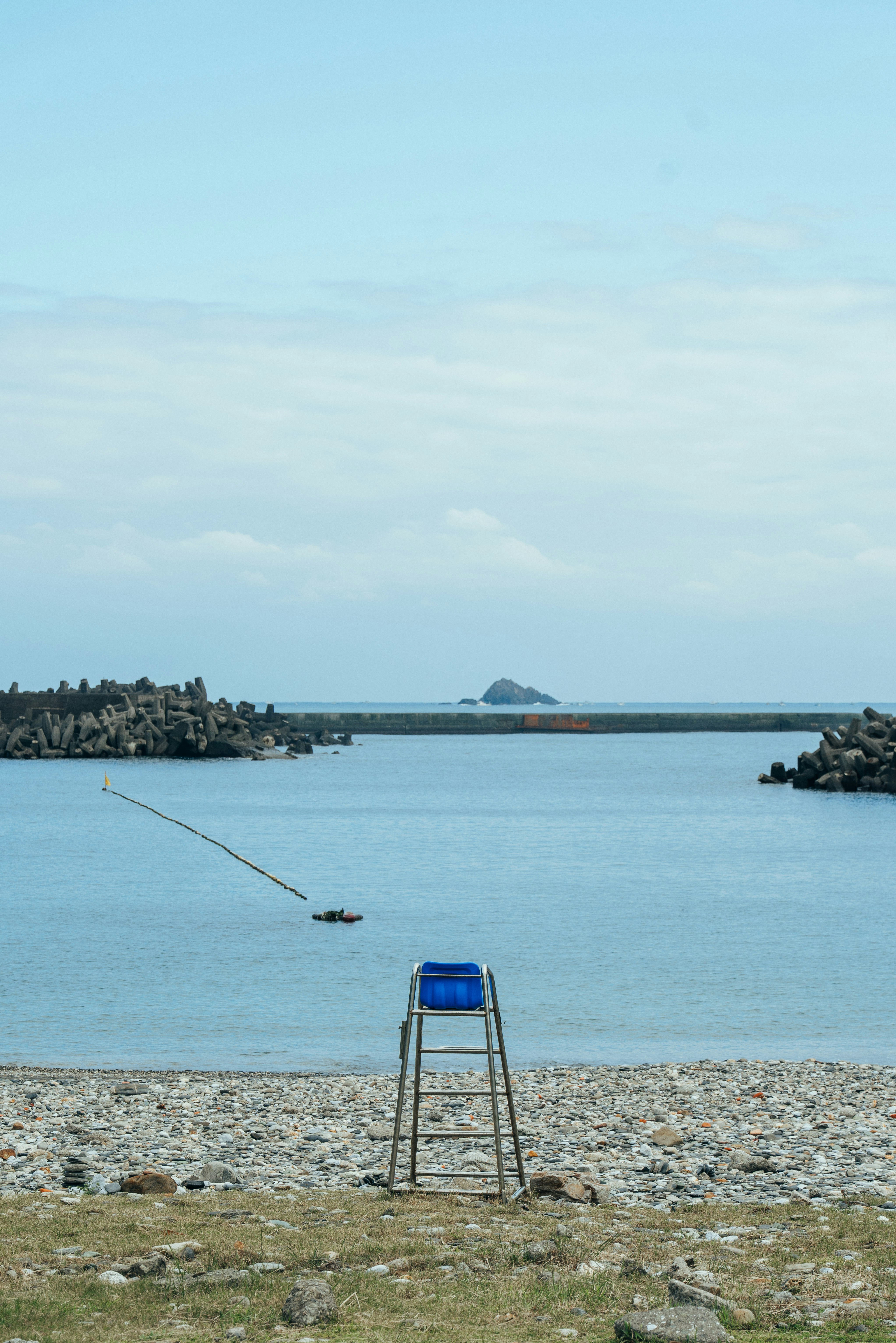 一把藍色椅子立在海灘上，背景是平靜的海洋