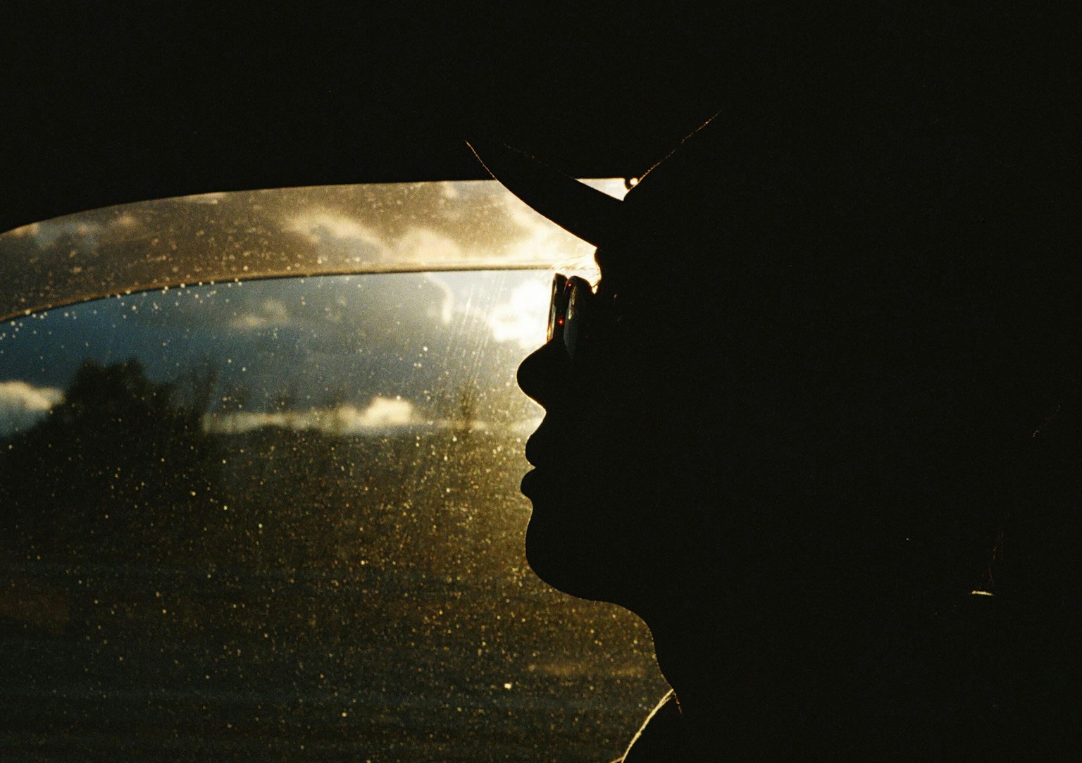 Silhouette einer Person im Auto mit Sonnenuntergangsreflexionen im Fenster