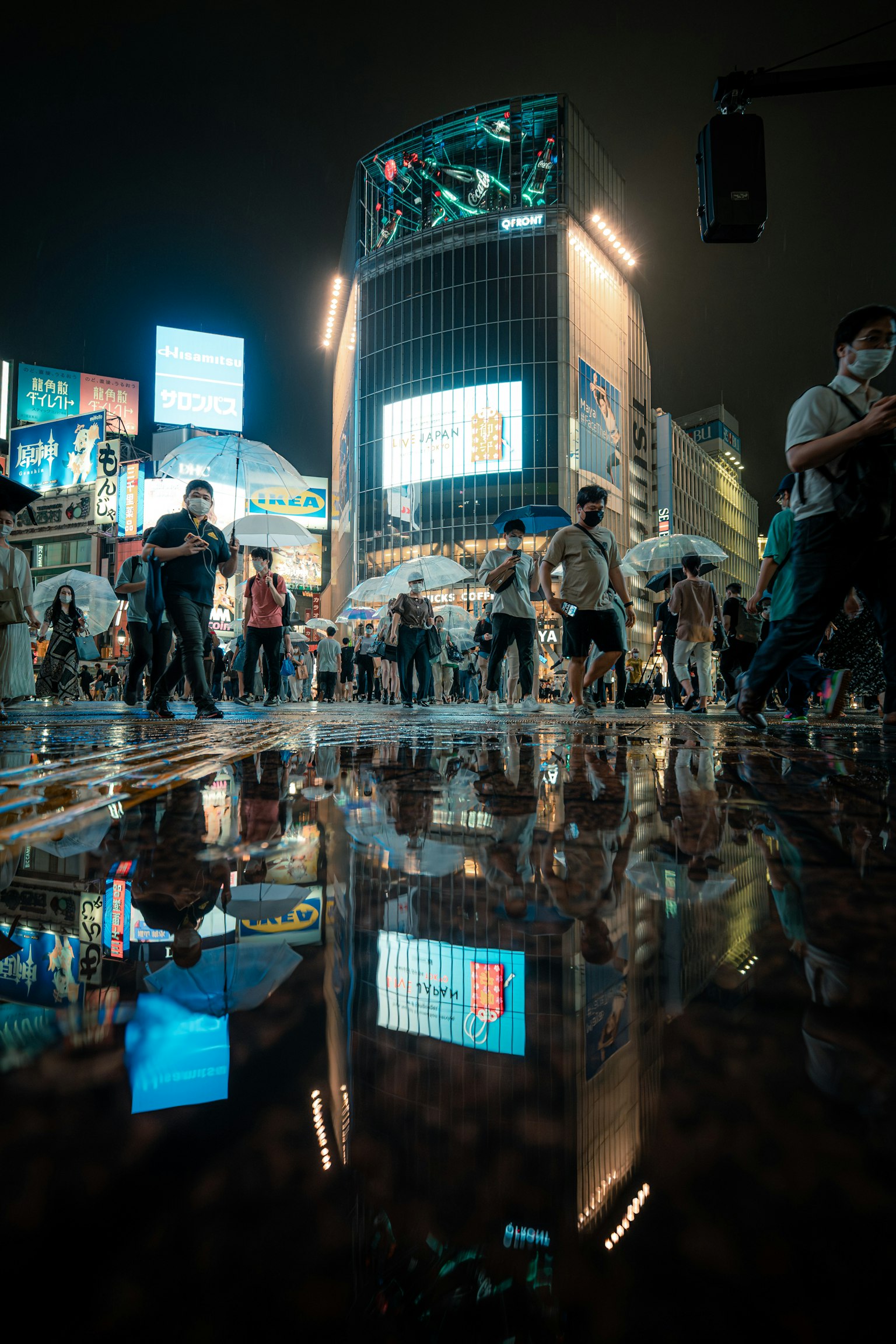 夜晚人们在涩谷交叉口穿行，水洼中的倒影