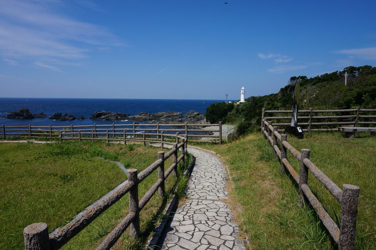 Chemin pittoresque à travers la prairie menant à l'océan avec un phare au loin