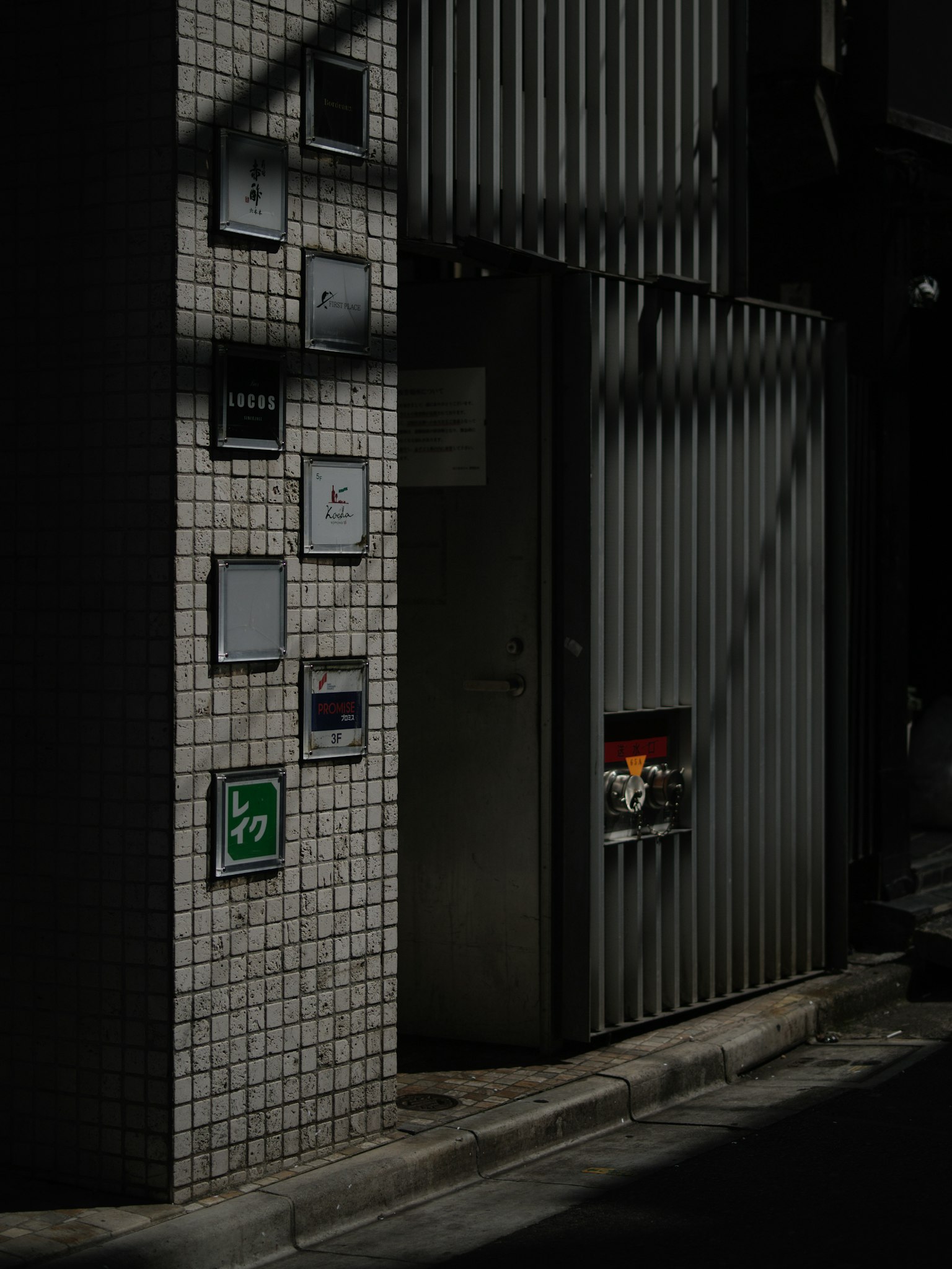Vicolo poco illuminato con una porta in metallo e segnali su parete piastrellata