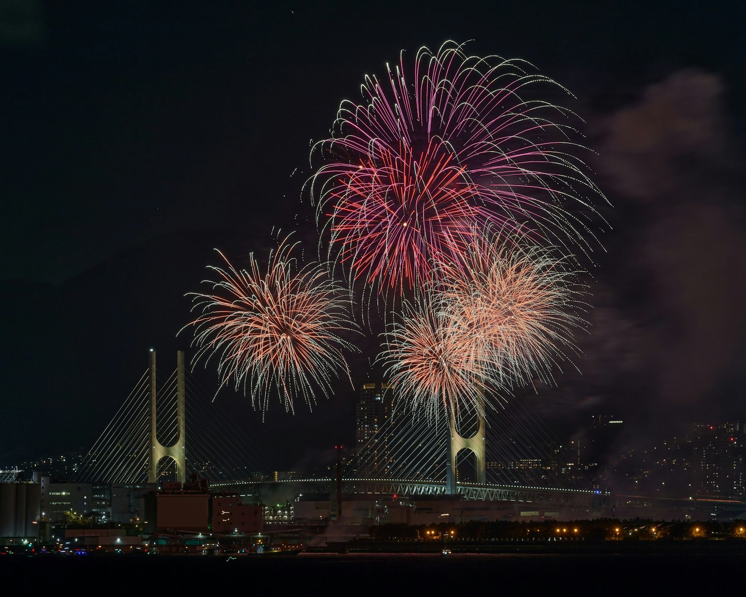 Fuegos artificiales coloridos estallando en el cielo nocturno con un puente de fondo