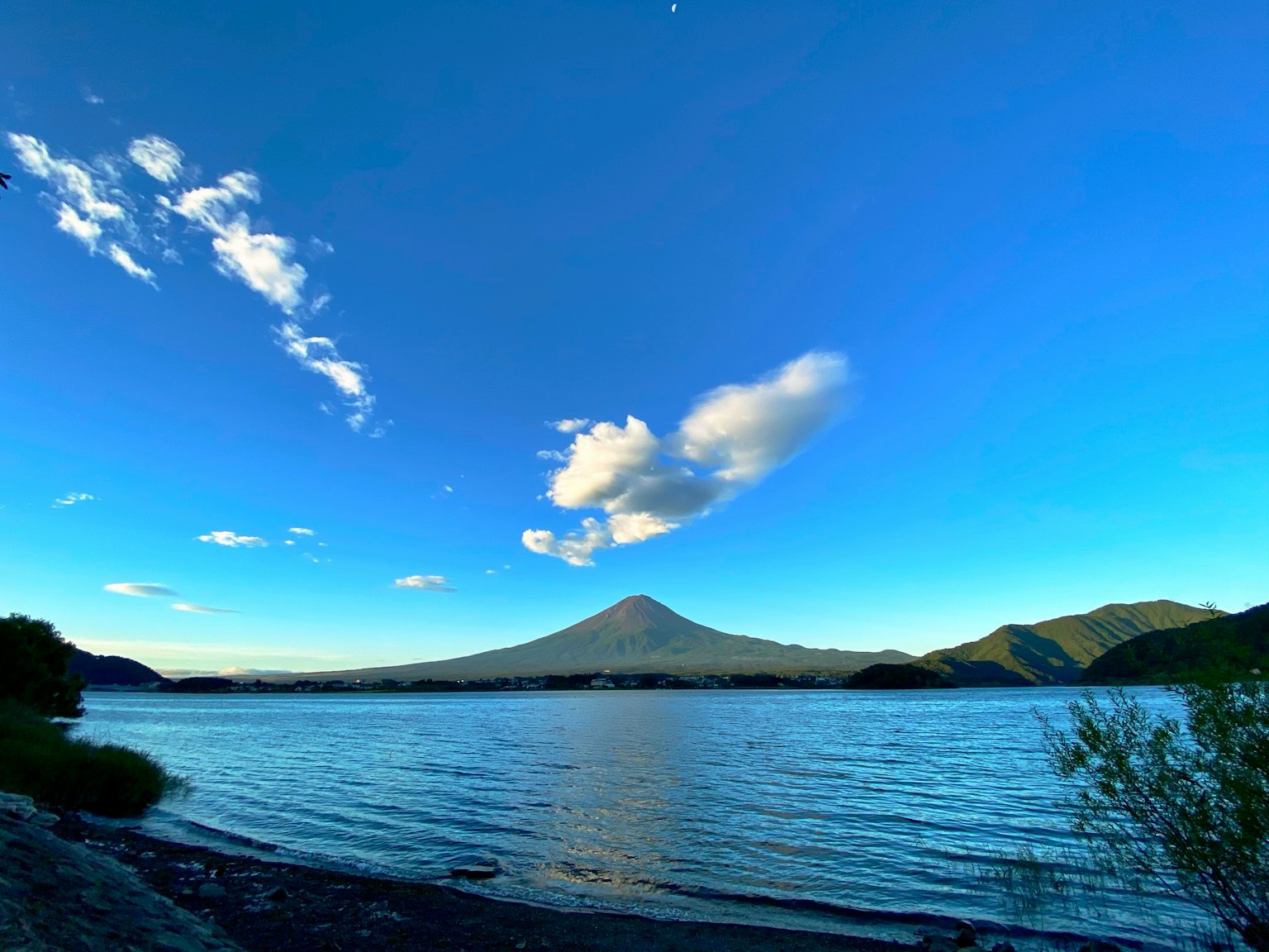 Un volcan se dressant au-dessus d'un lac sous un ciel bleu clair et des nuages