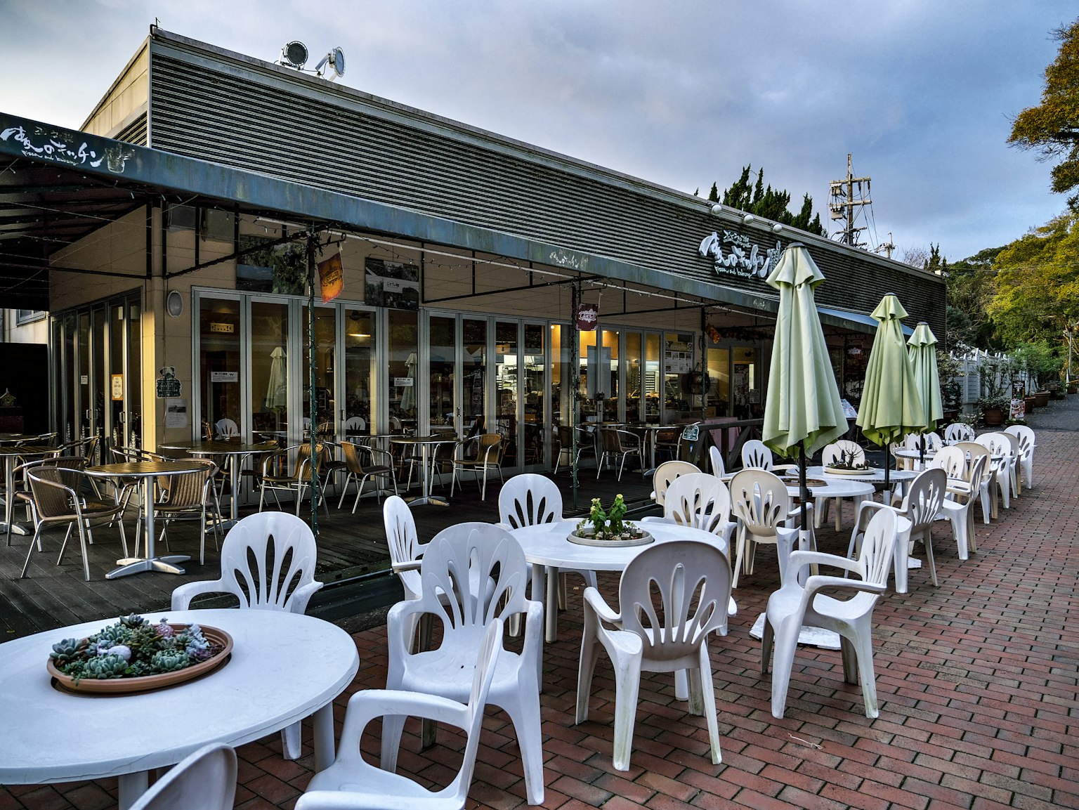 Außenansicht eines Cafés mit Terrassensitzplätzen und weißen Plastikstühlen