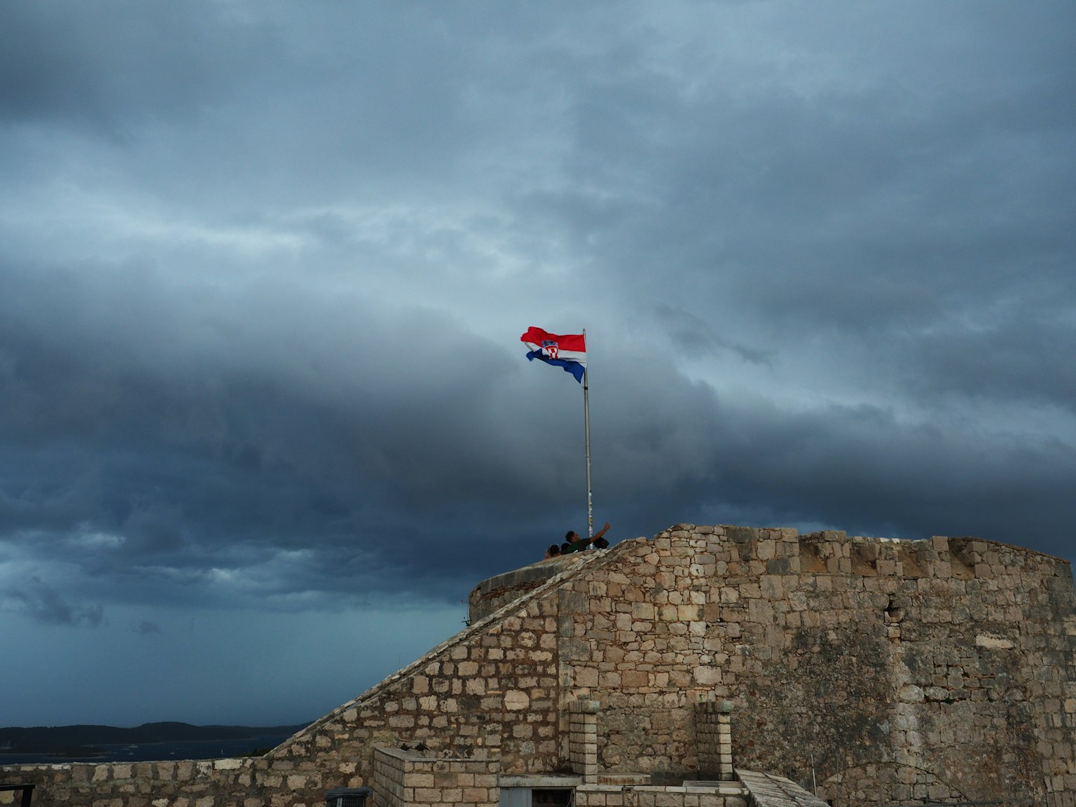 Bandera croata ondeando en la cima de una fortaleza de piedra bajo un cielo nublado