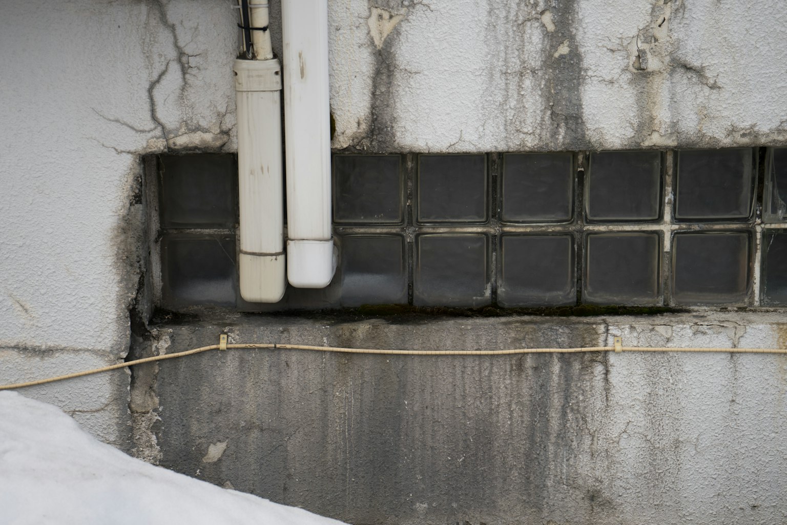 Structure with glass block window and pipes at the bottom of a white wall