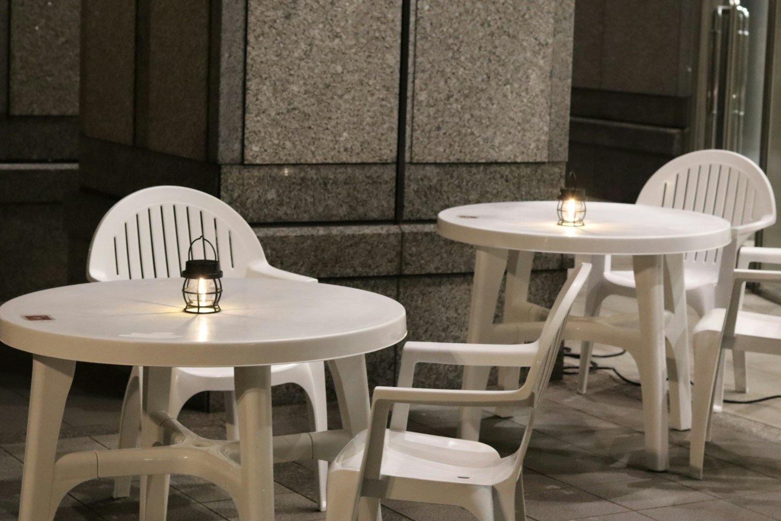 白いプラスチックのテーブルと椅子が並ぶ夜のカフェの外観