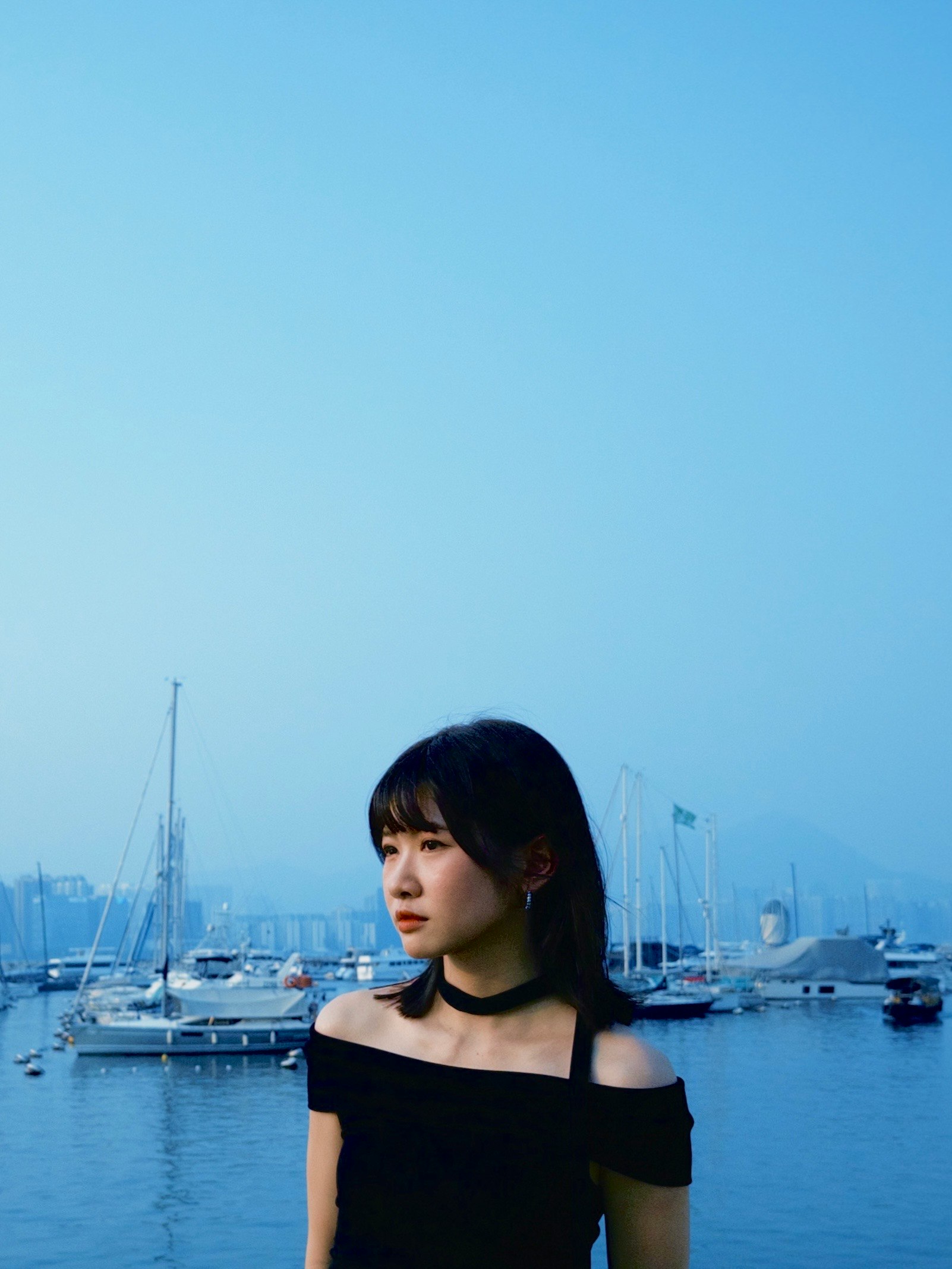 港のヨットを背景にした黒いオフショルの女性