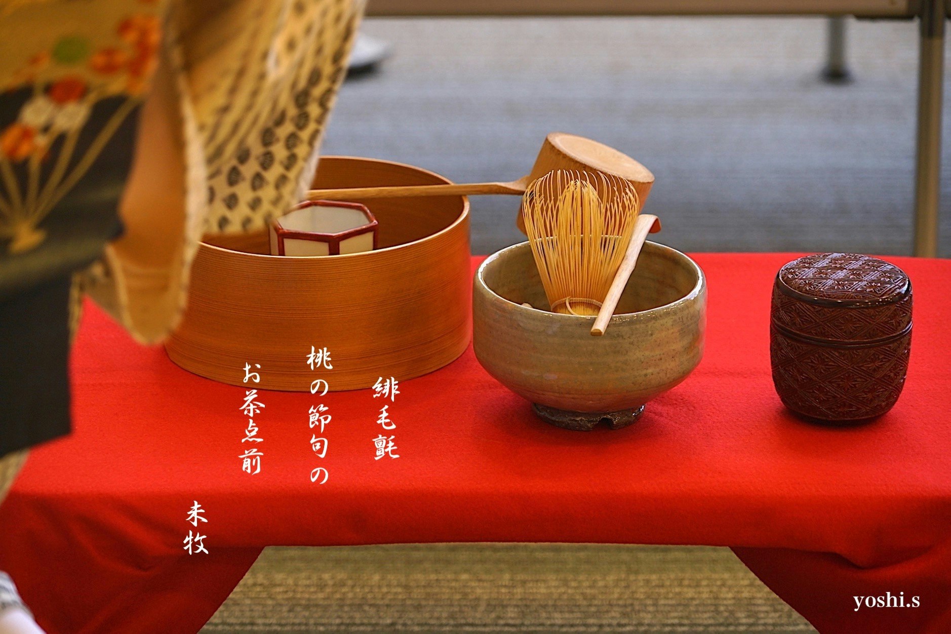 茶道の道具が並ぶ赤い布の上に置かれた木製の茶碗と茶筅
