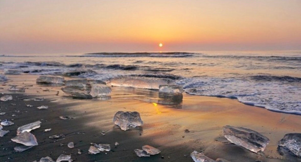 大津海岸の夕焼けと打ち寄せる波、砂浜に転がる岩