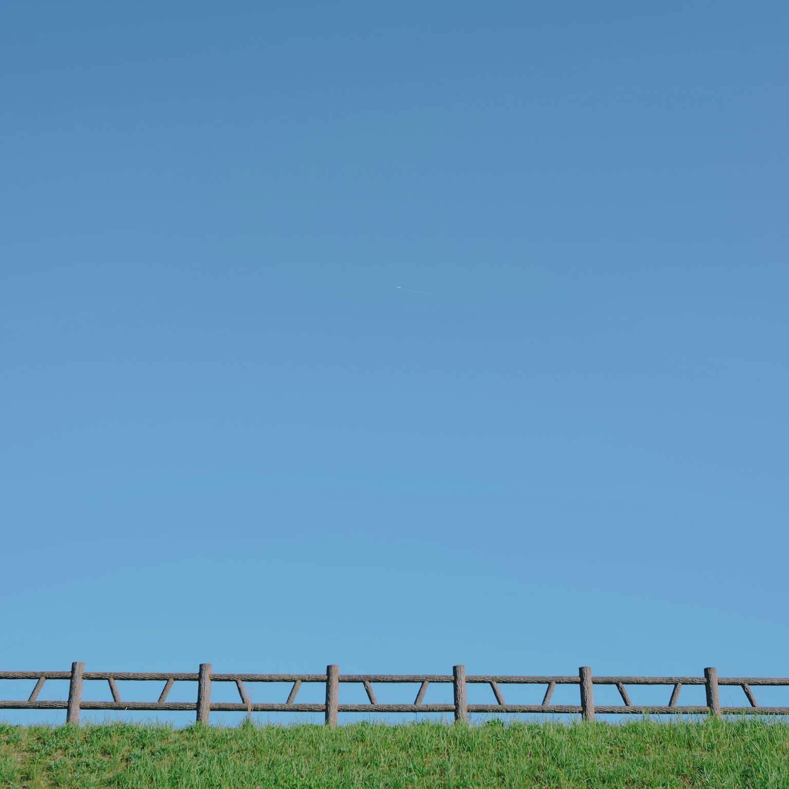 Valla de madera a lo largo de hierba verde bajo un cielo azul claro