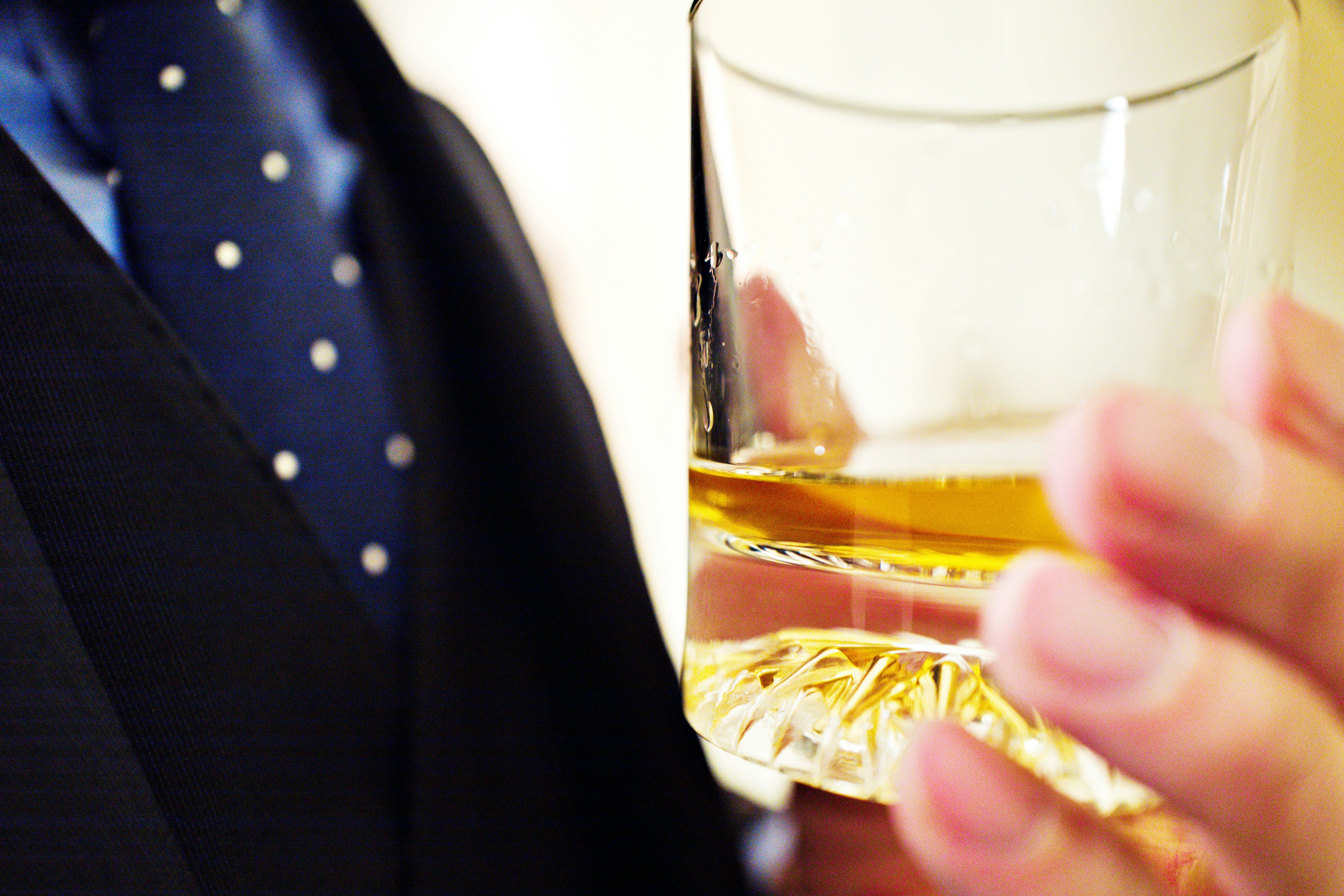 A person in a suit holding a glass as a drink is poured