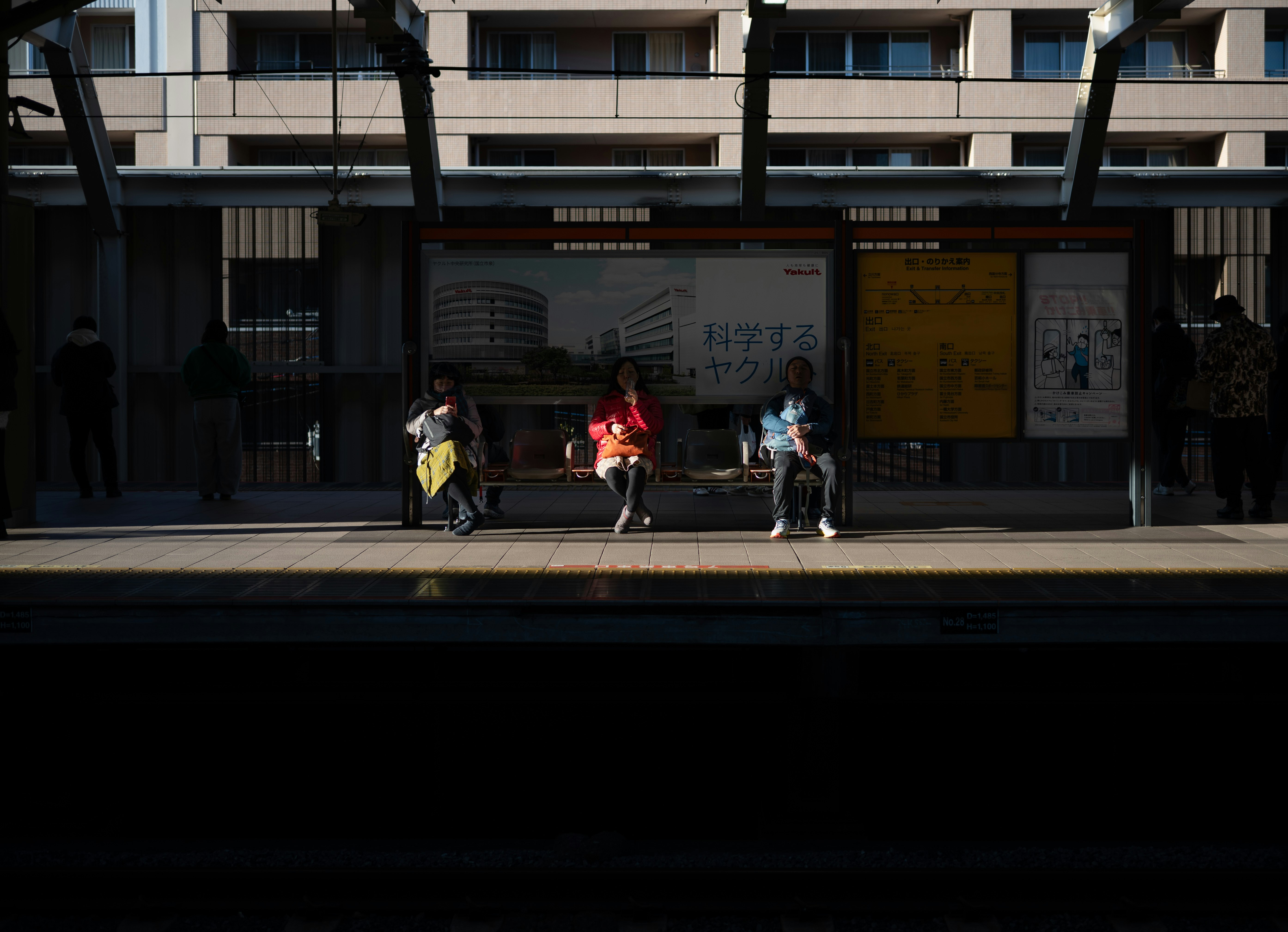 people resting on a bench by a storefront-lined street near a station