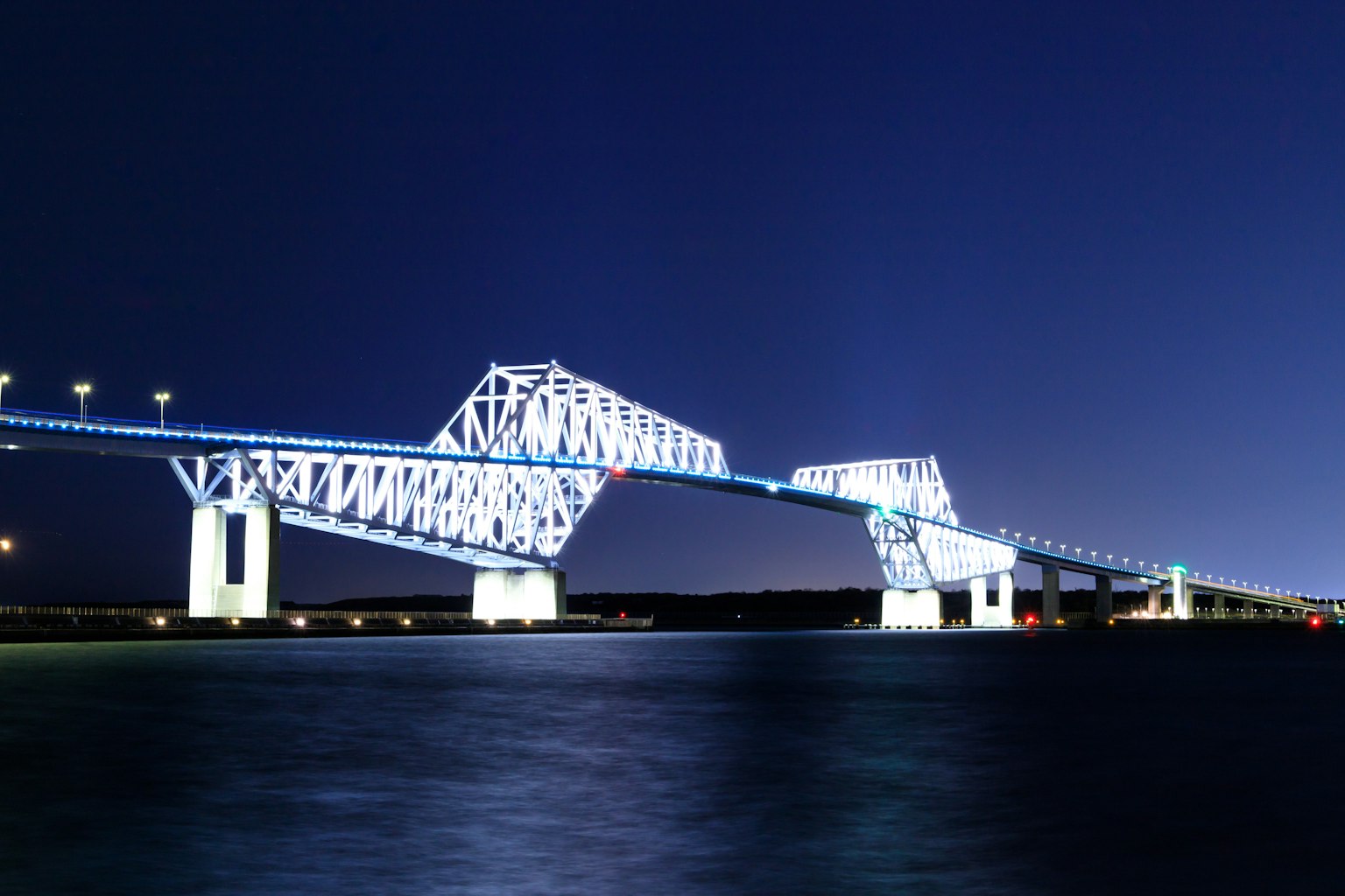 Bridge structure illuminated at night against a blue sky