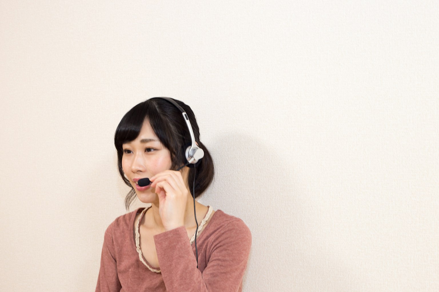 A woman wearing a headset speaking against a plain background