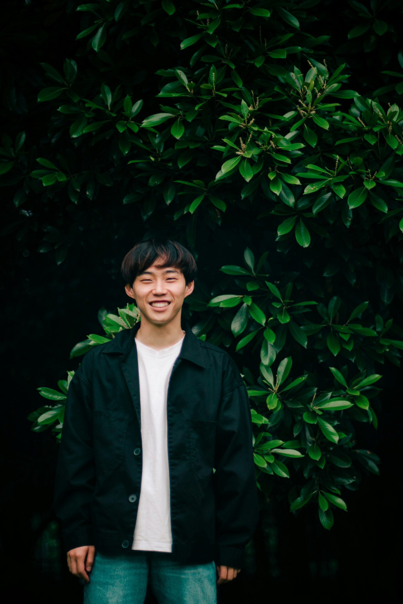 微笑的年輕男性站在綠色葉子背景前