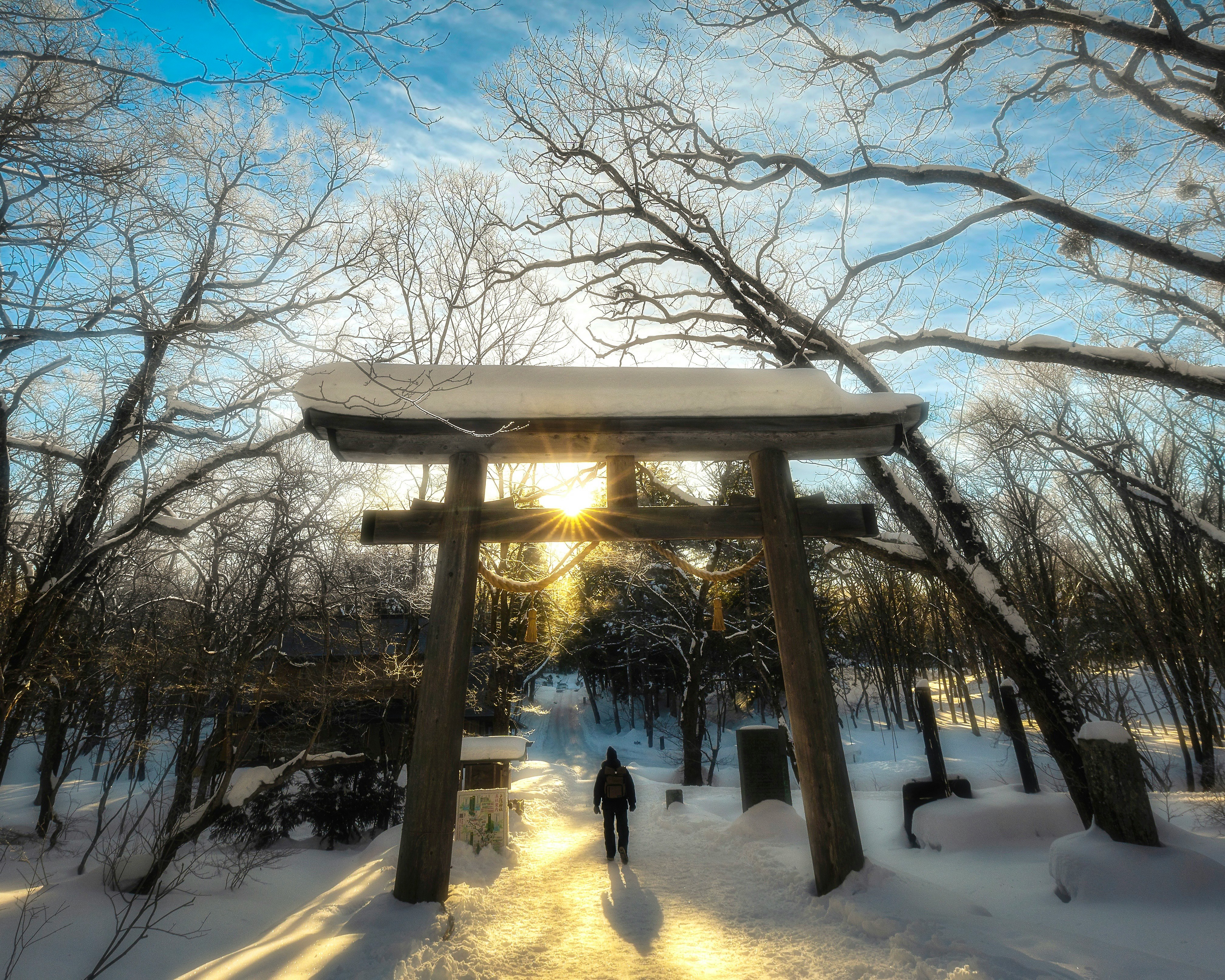silhouette marchant sous un torii sur un chemin enneigé