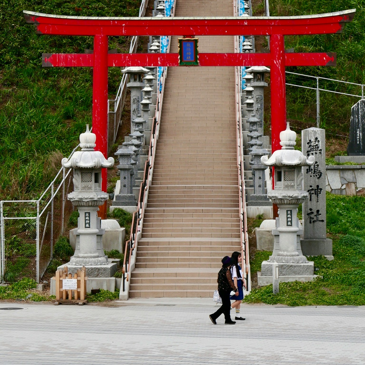 Cổng torii màu đỏ với đèn đá bên cạnh cầu thang và người đi bộ