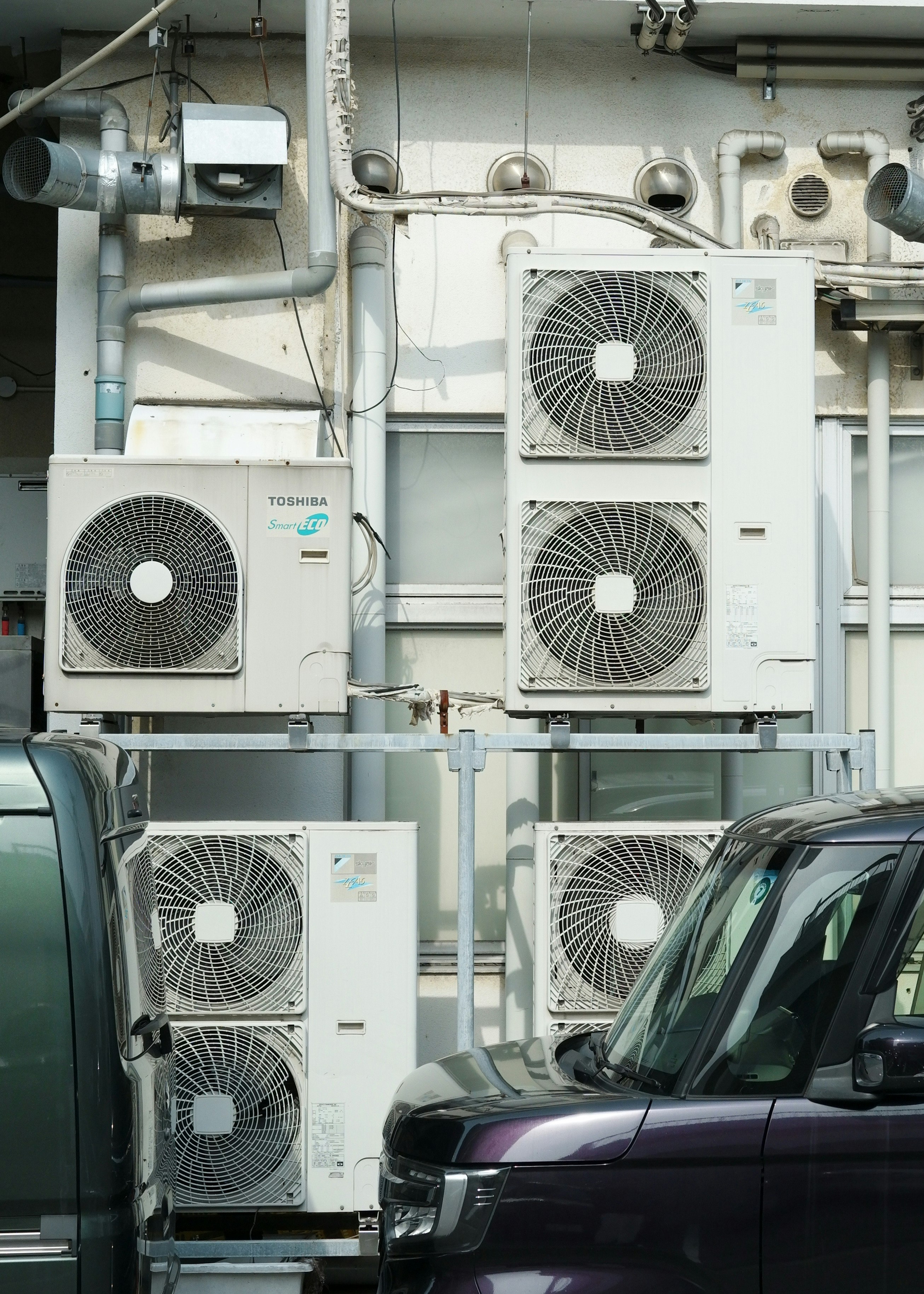 Deretan unit AC outdoor dengan sebuah mobil