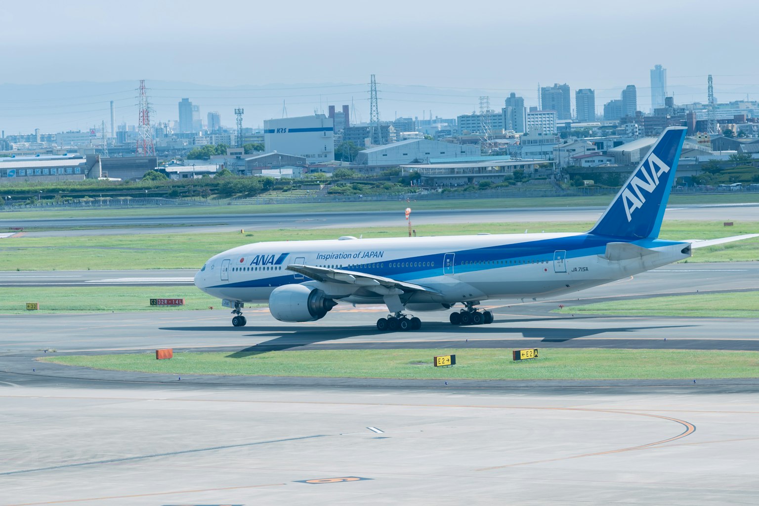 ANA-Flugzeug rollt auf der Startbahn mit einer Stadtansicht im Hintergrund