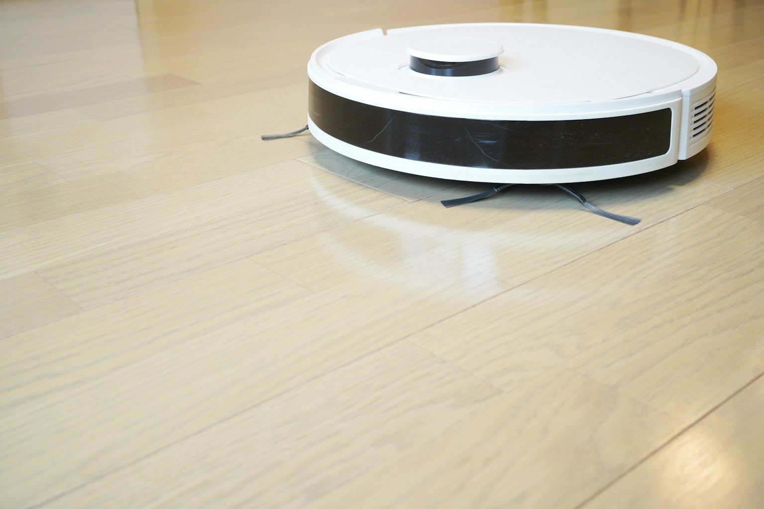Aspirateur robot blanc se déplaçant sur un sol en bois