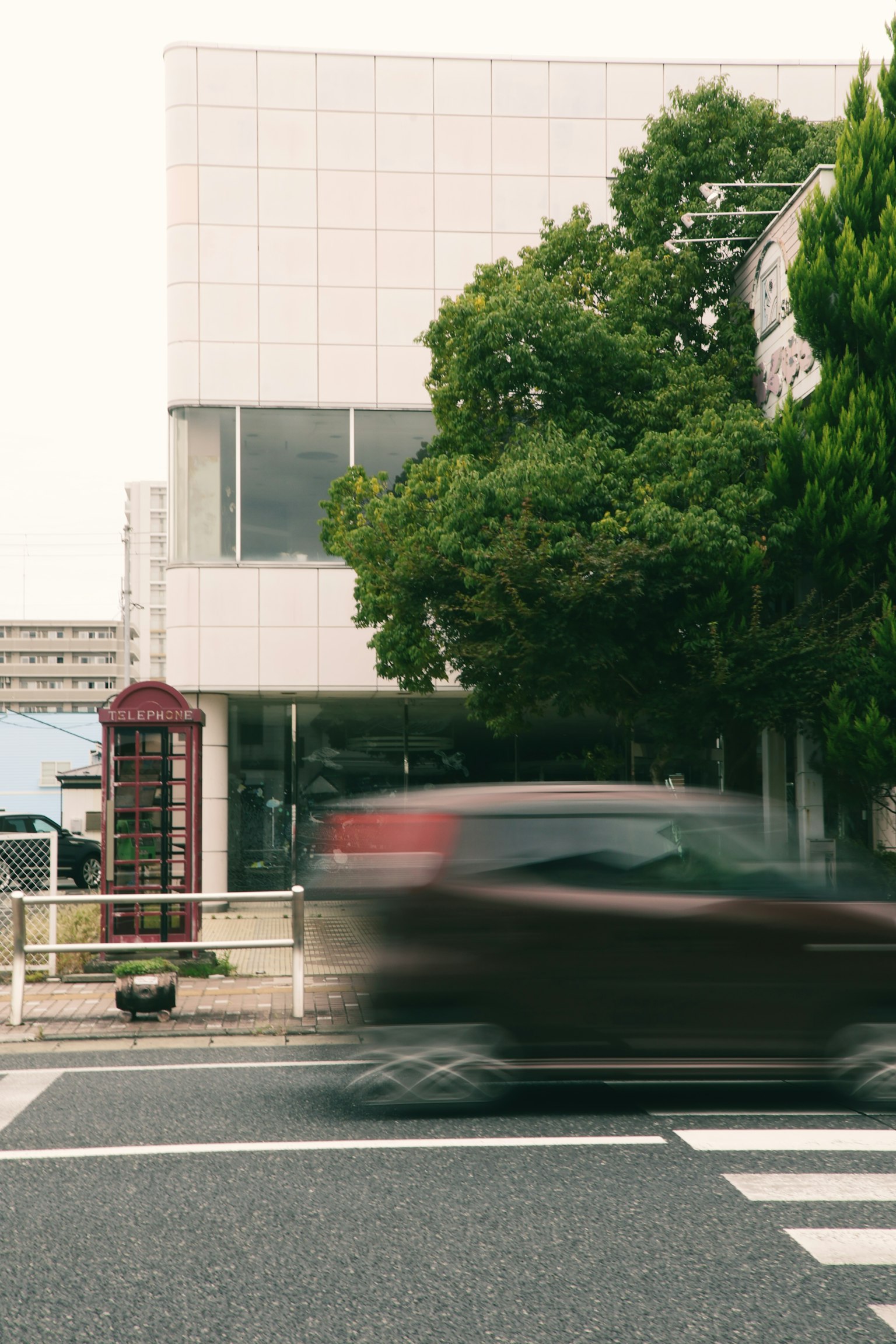 白い建物と緑の木がある通りの風景 車が通り過ぎる