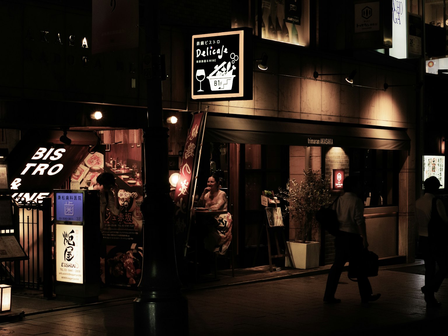 Außenansicht eines Bistros bei Nacht mit vorbeigehenden Menschen