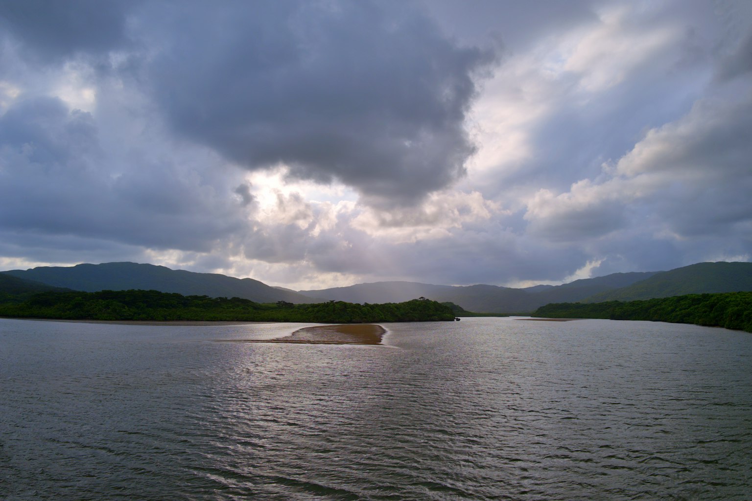 Pemandangan danau yang tenang dengan pegunungan di bawah langit mendung dan refleksi air