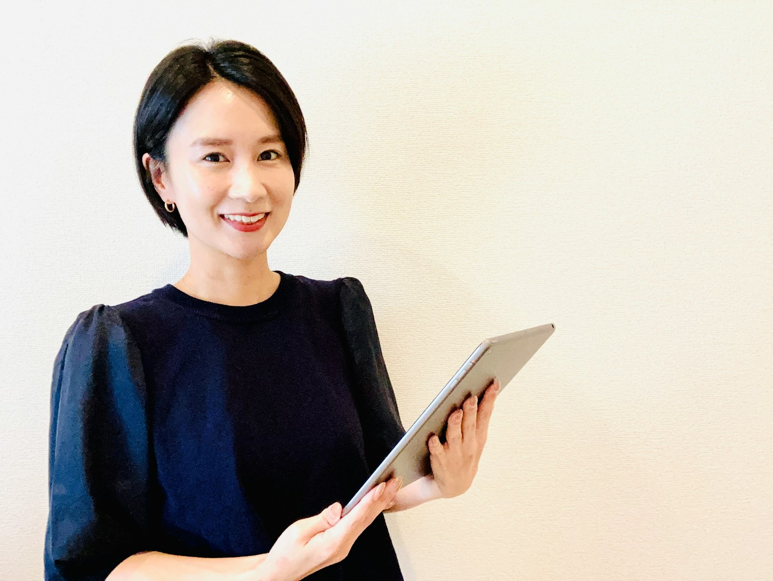Người phụ nữ mỉm cười trong khi cầm máy tính bảng trước nền đơn giản