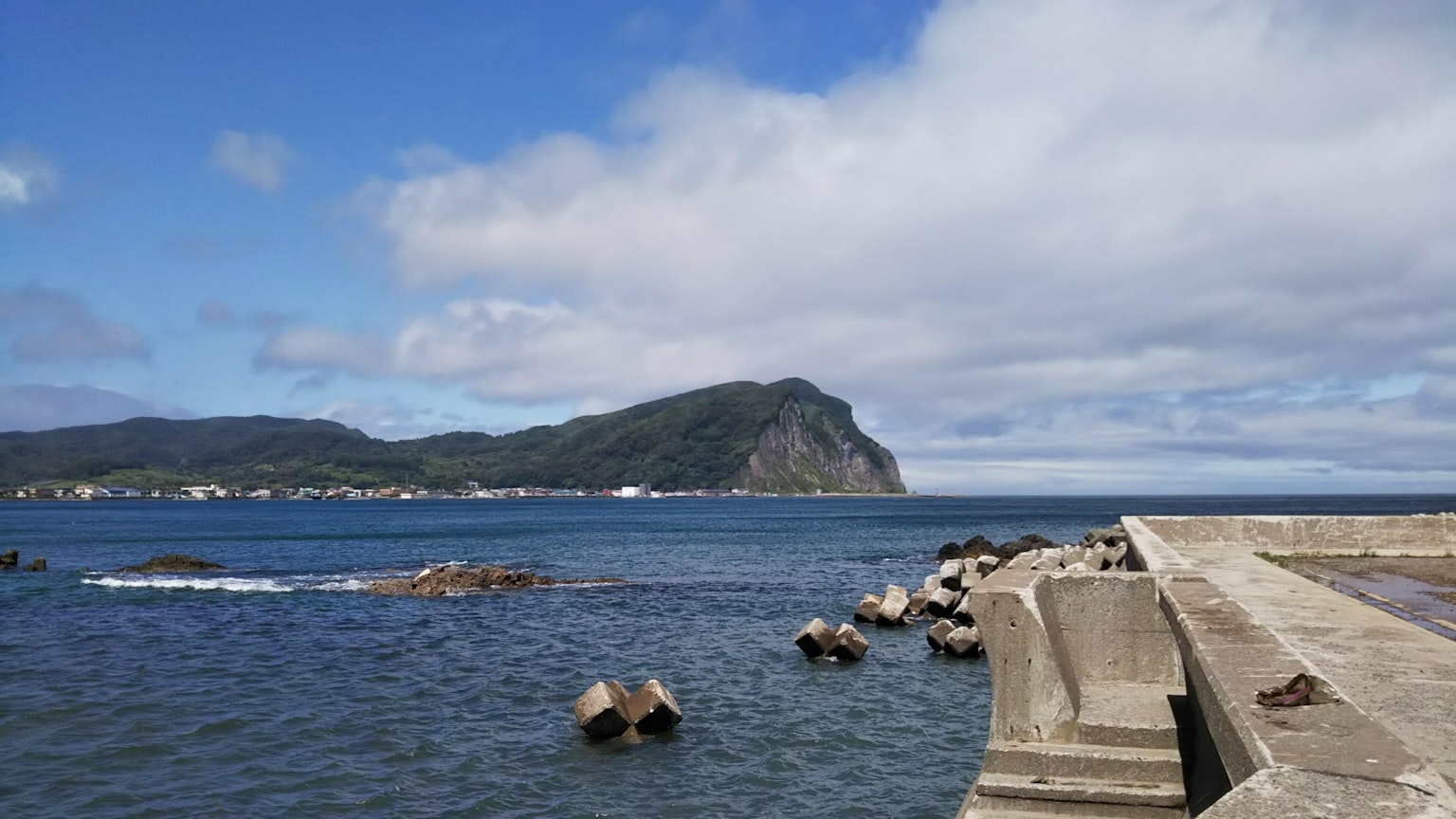 Scenic view of blue sea and sky with a distant mountain visible and a concrete pier