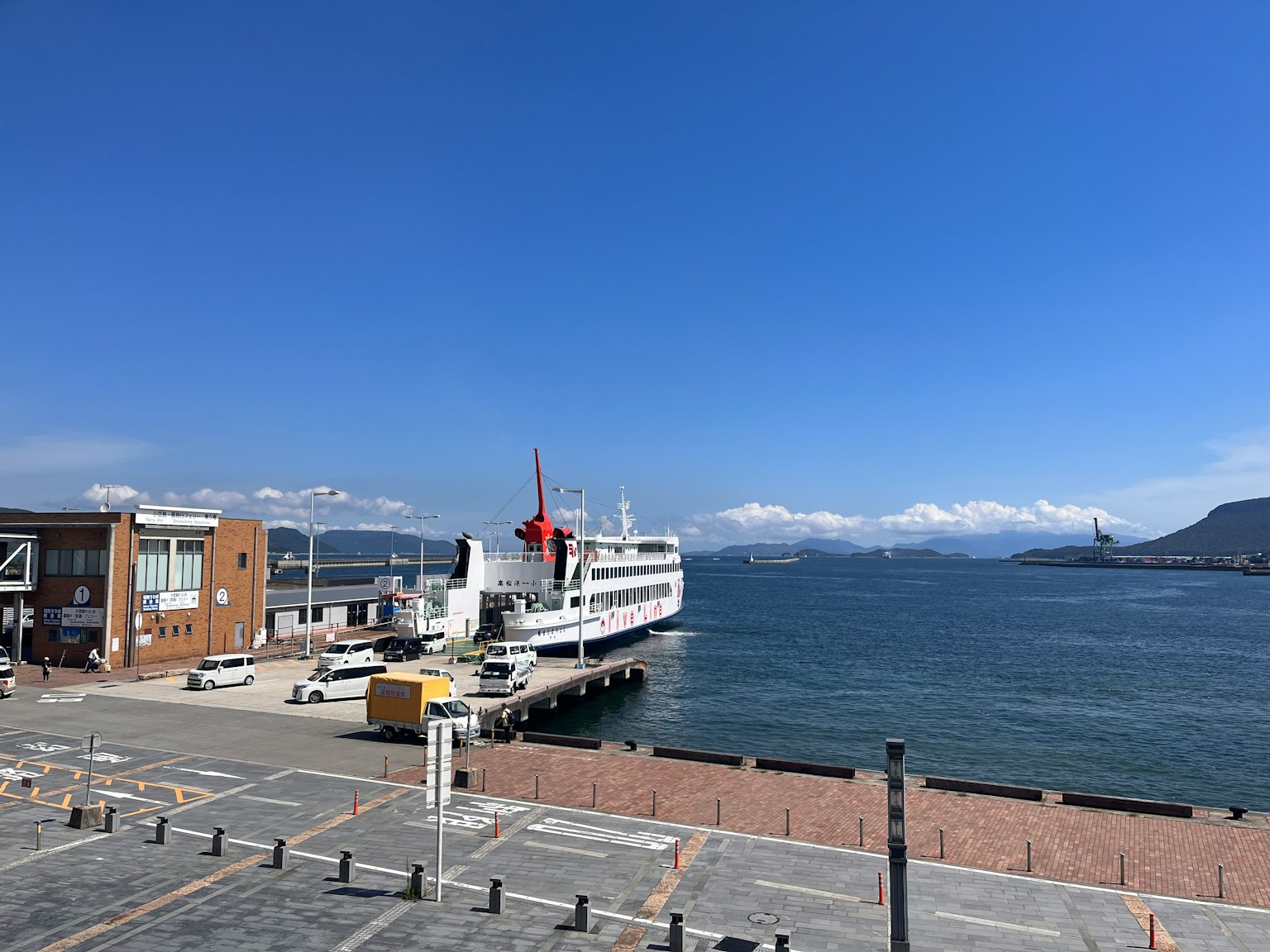 Scène de port avec un ferry blanc et un drapeau rouge sous un ciel bleu clair